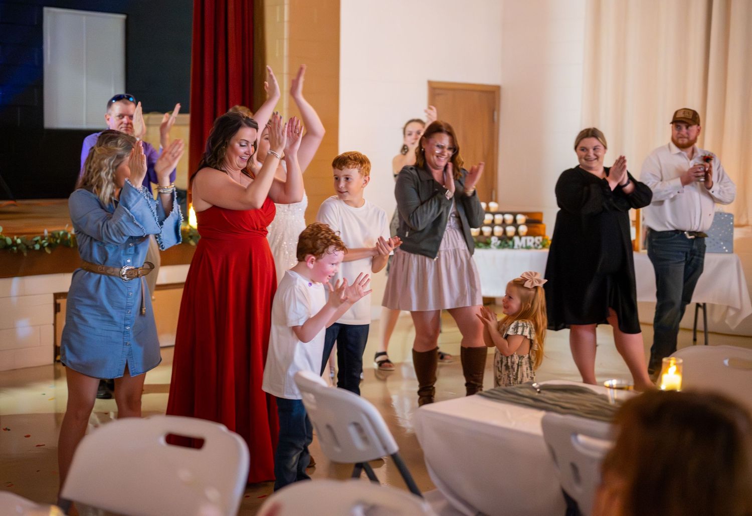 Wedding reception guests dancing and celebrating in an indoor venue with red curtains.