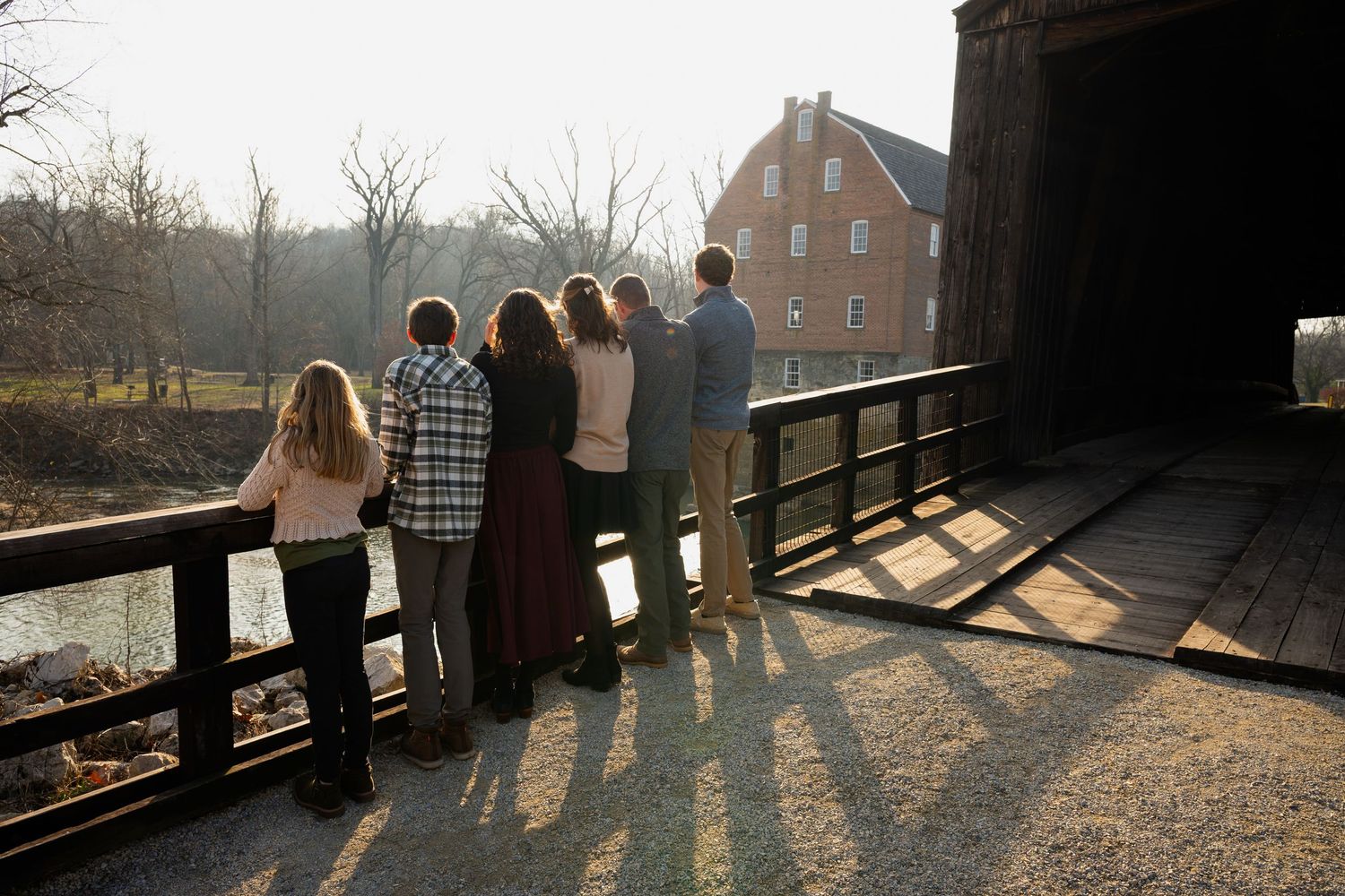 Group standing on a rustic wooden bridge surrounded by autumn trees at sunset.