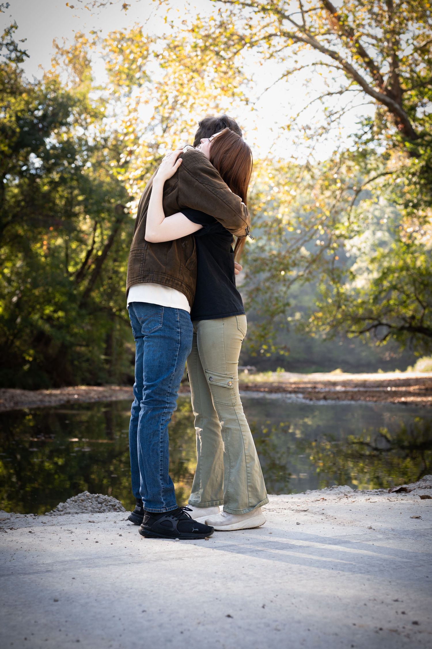 Couple sitting together on a snowy rock in a wooded area during autumn with golden leaves in the background.