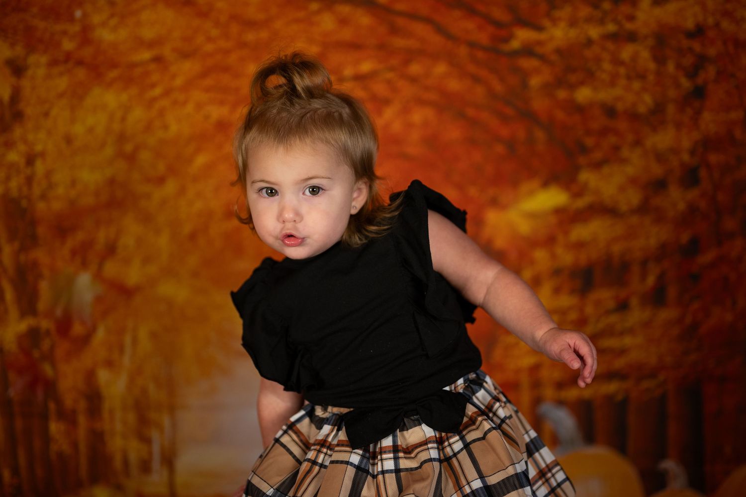 A small child in a black top and plaid skirt twirls against an autumn-themed backdrop.