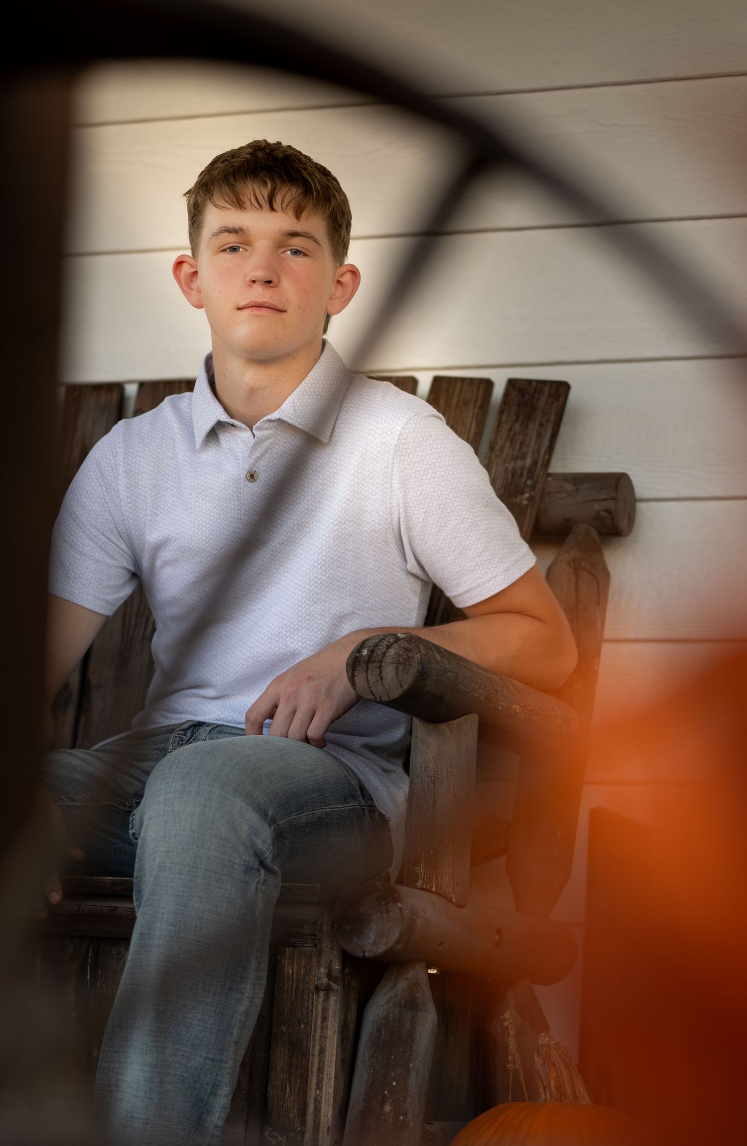 A person in a white polo shirt and jeans sits on a wooden bench against a light-colored wall.