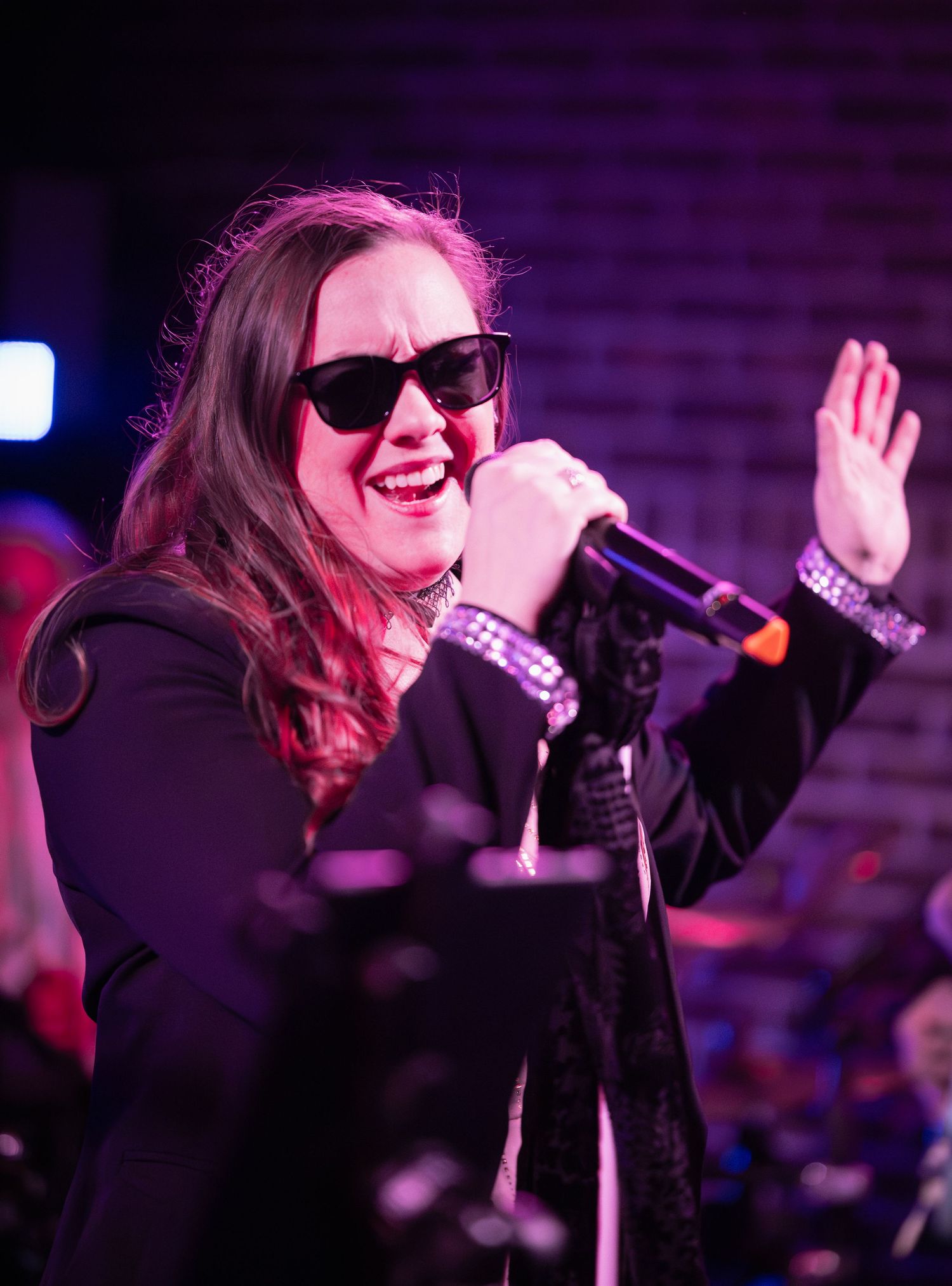 A performer in black attire sings passionately on stage under purple lighting during a live concert performance.