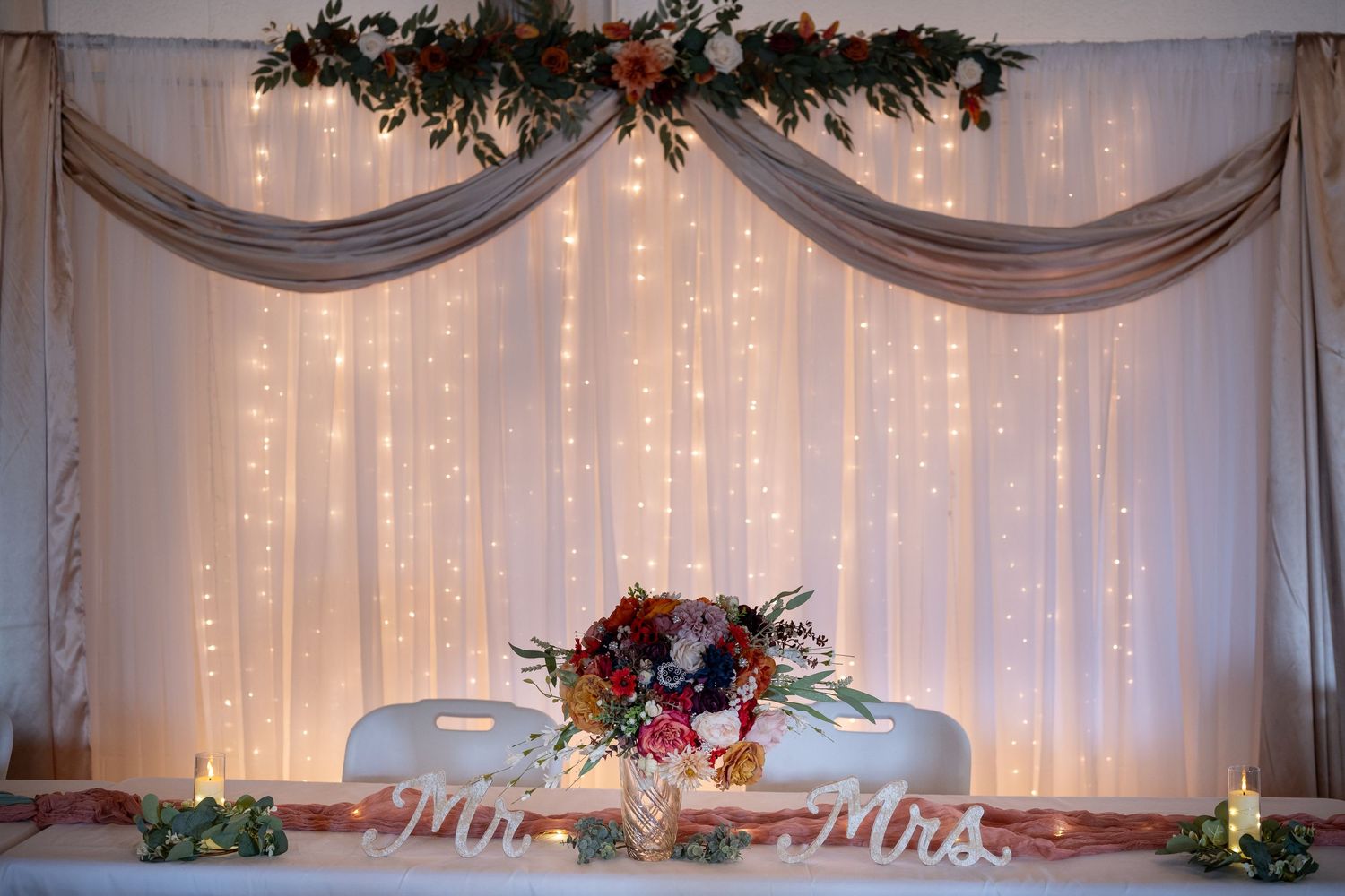 Wedding backdrop with white draping, twinkle lights and floral garland decorations.