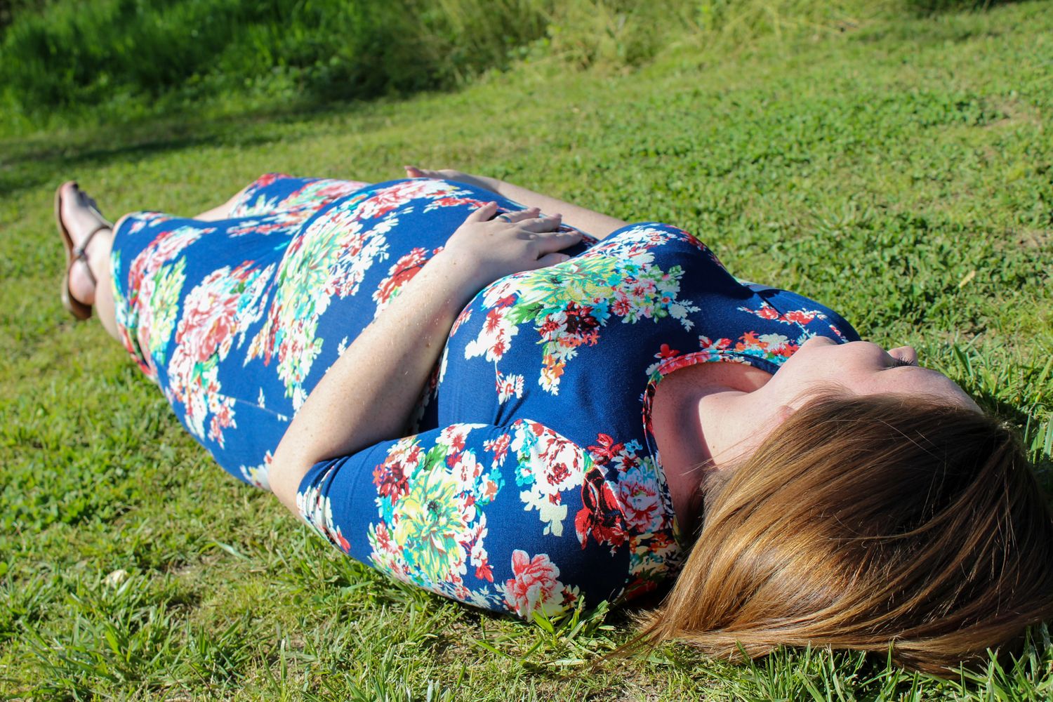 A person in a floral dress lies peacefully on a grassy lawn on a sunny day.