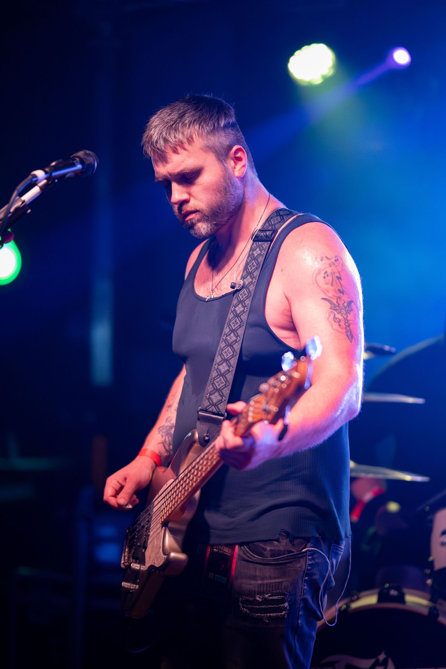 Bass guitarist performs on stage with dramatic blue lighting and visible tattoos during a live concert performance.