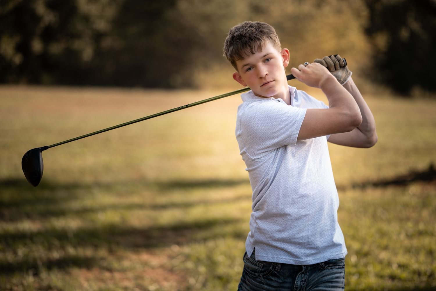 A golfer in a white shirt practices their swing during a sunset session on a golf course.