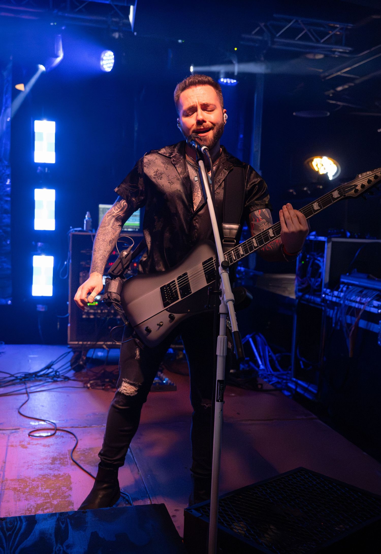 Musician performs on stage with guitar in dark blue lighting at live music venue during concert performance.