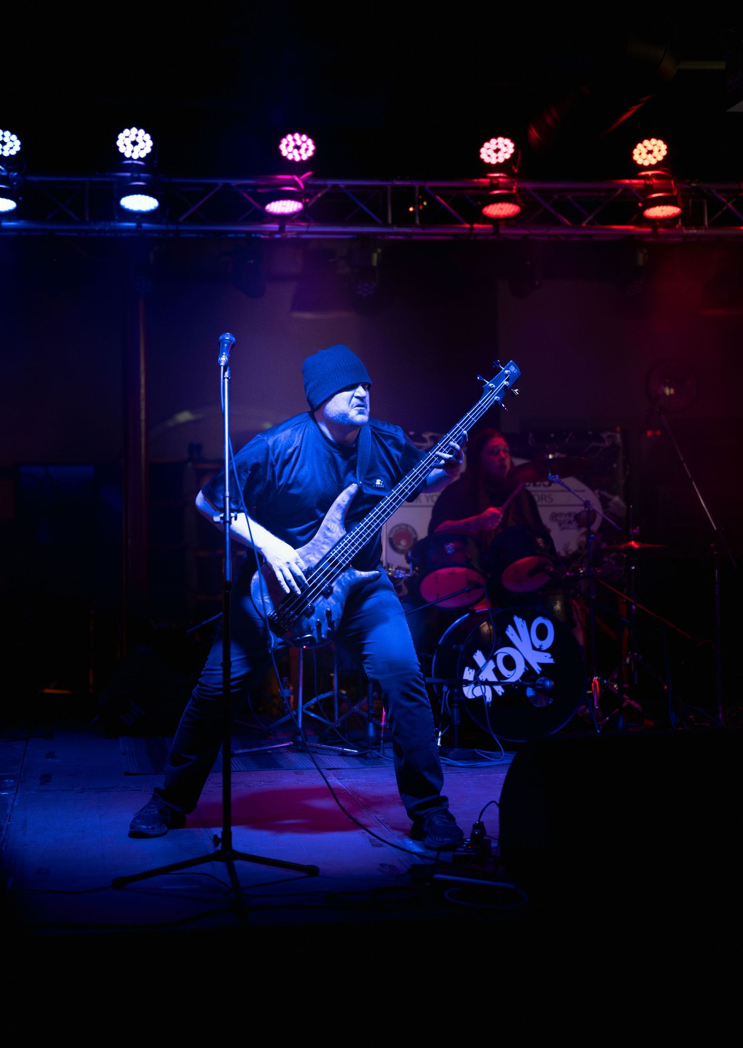 Musician performs on stage with guitar under dramatic blue and red lighting during live concert performance.