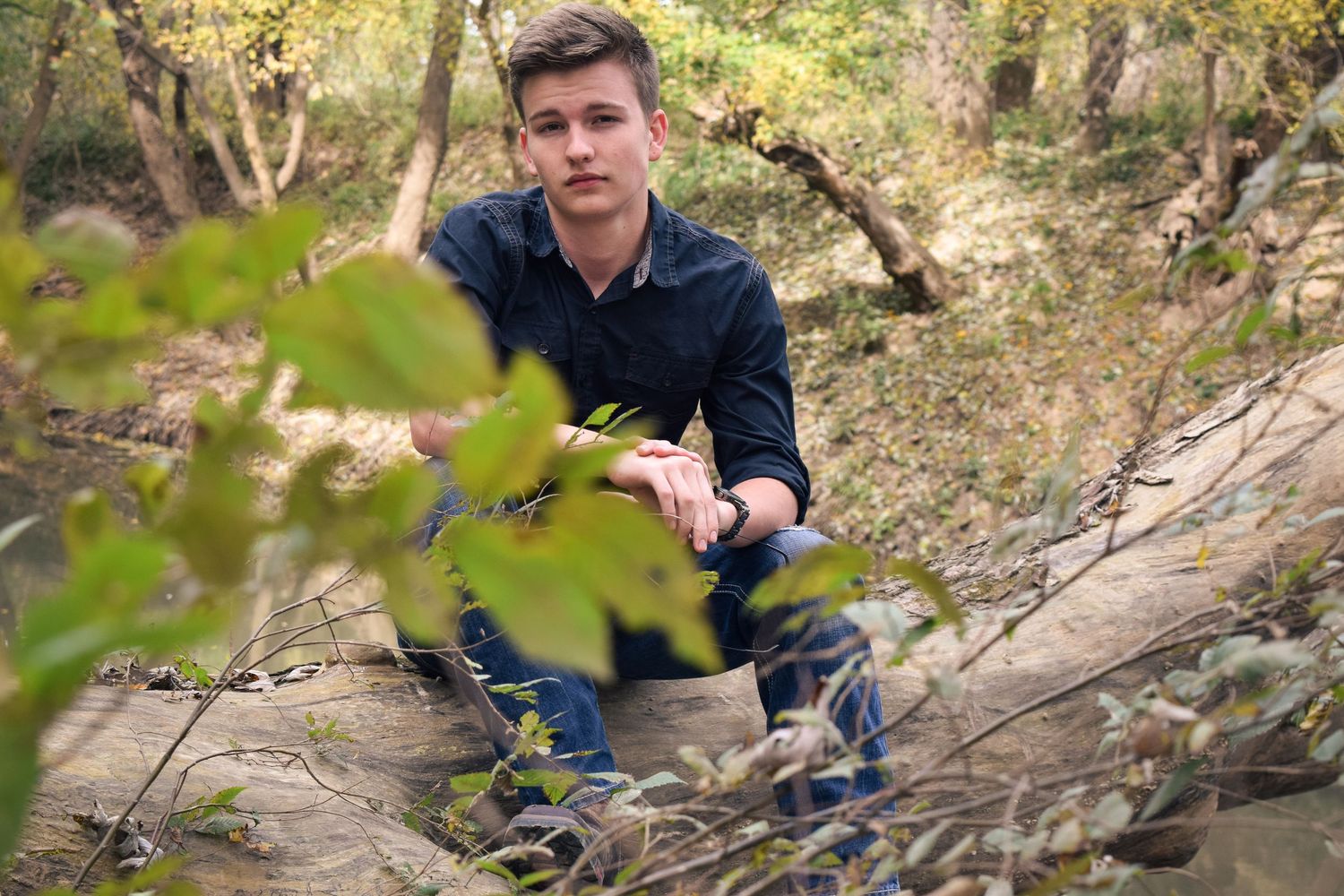Person in dark clothing sits on rocky terrain in a wooded outdoor setting during autumn season.