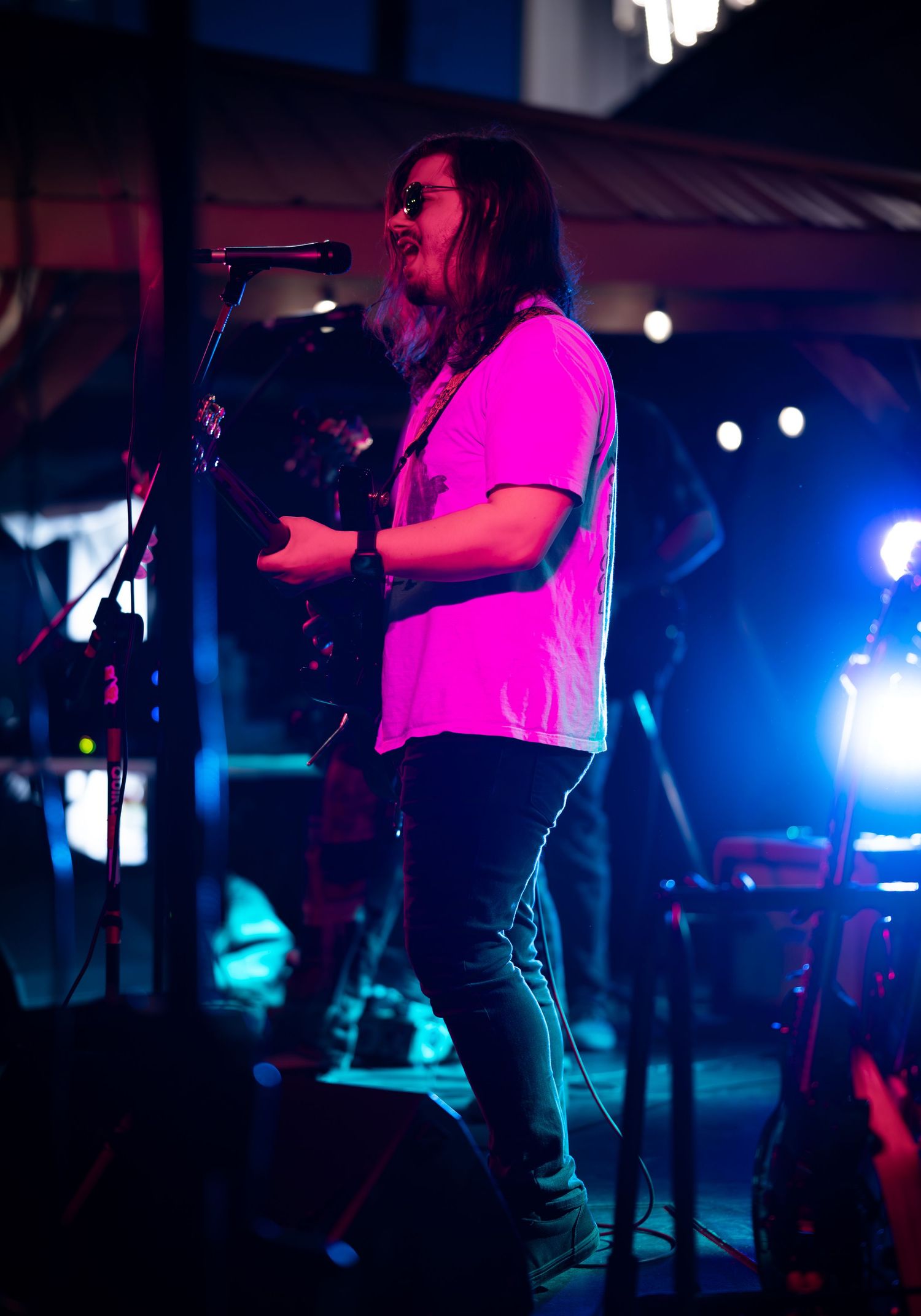Concert performer singing on stage illuminated by vibrant pink and blue lighting during a live music performance.