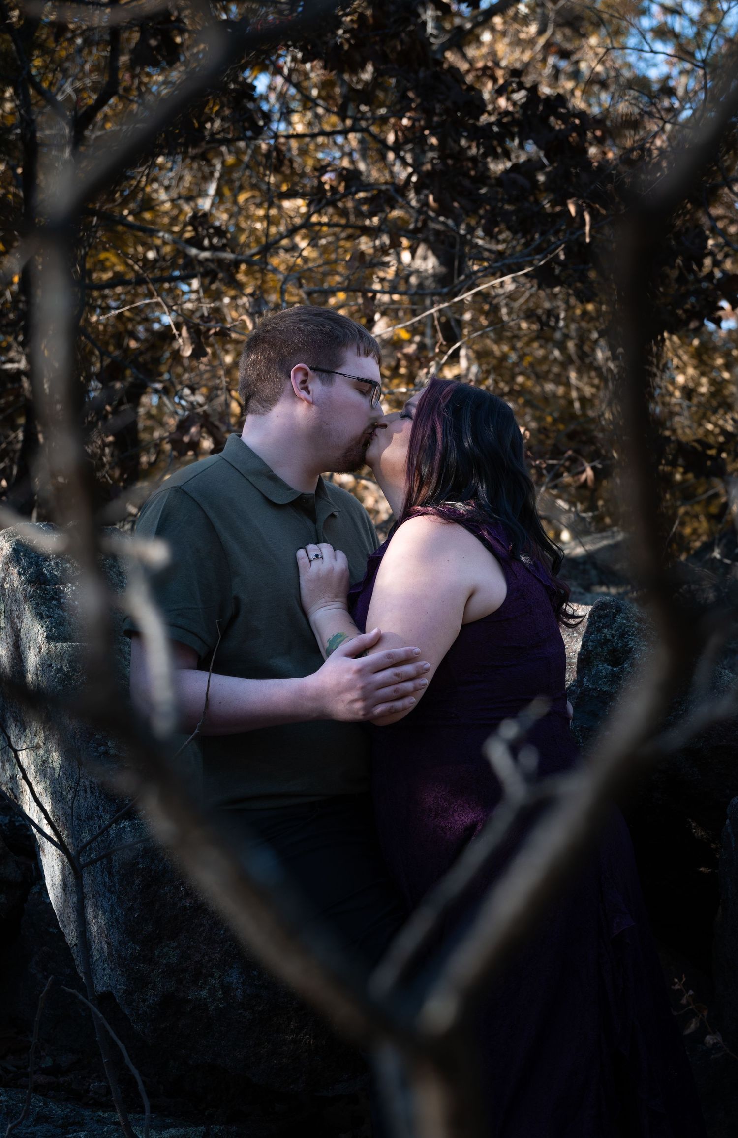 A romantic couple shares a tender embrace in a wooded setting during autumn with golden leaves in the background.