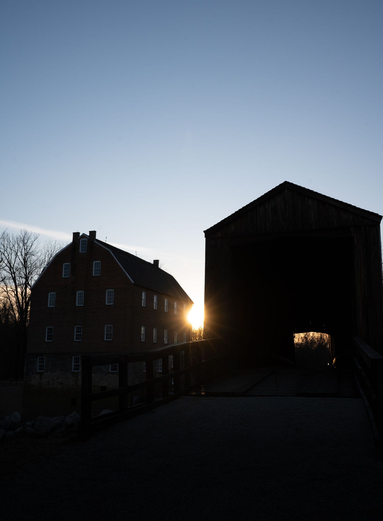 A sequence of silhouetted brick houses against a sunset sky with the sun peeking through creating a dramatic backlit effect.