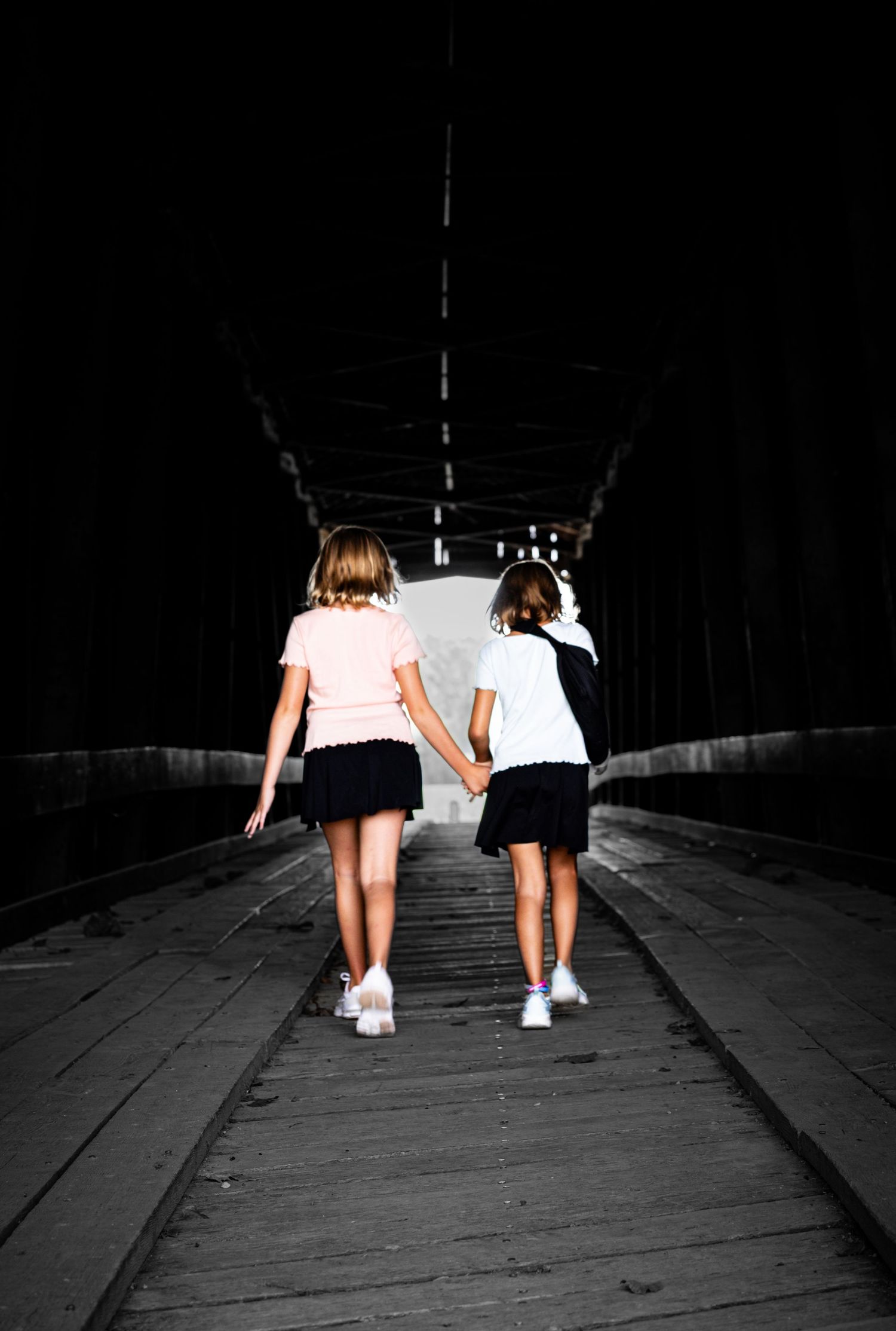 Two figures in light colored clothing walk together down a dark path in a dramatic black and white composition.