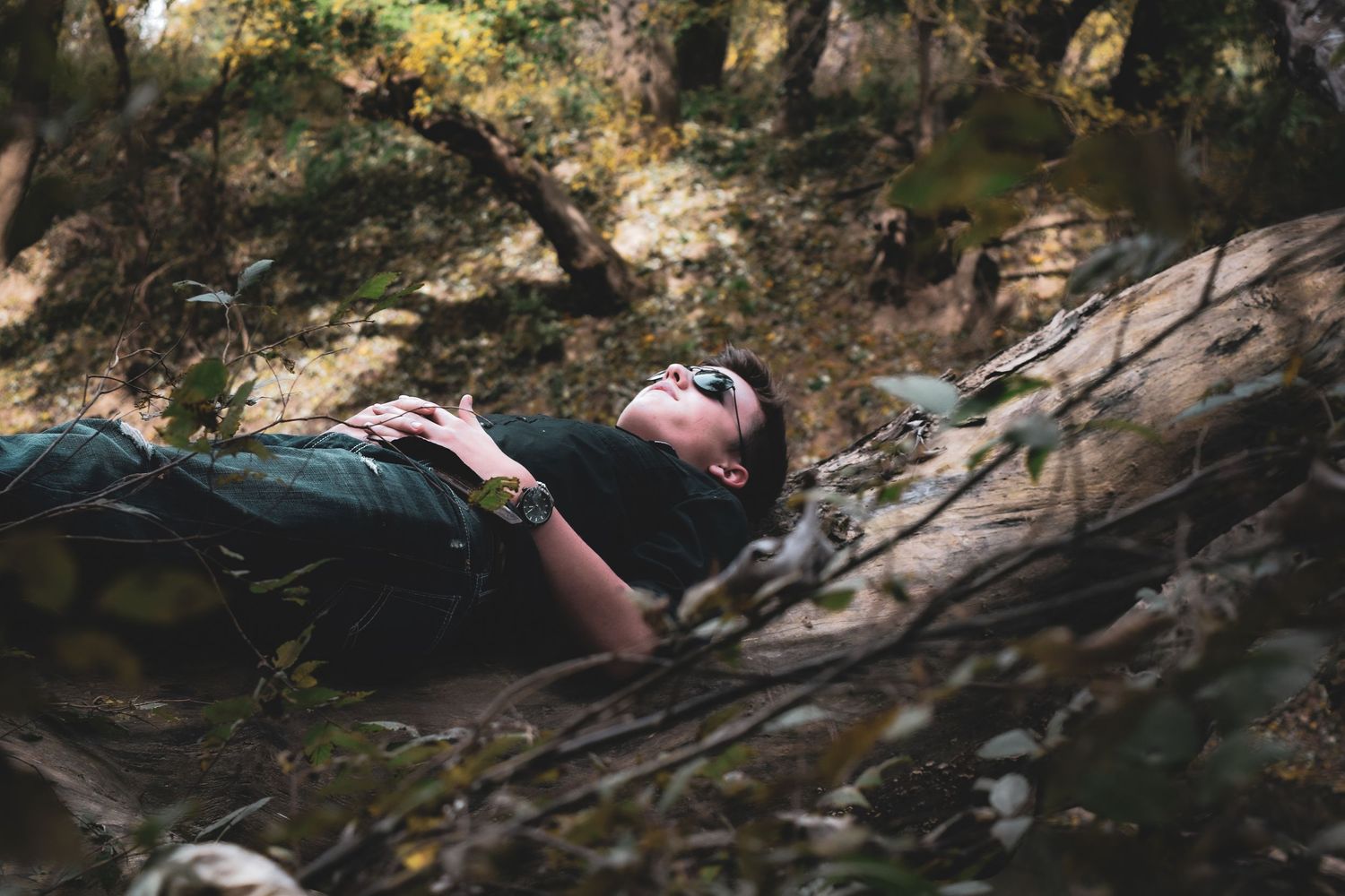 A person lies back on mossy rocks near a stream in a peaceful forest setting.