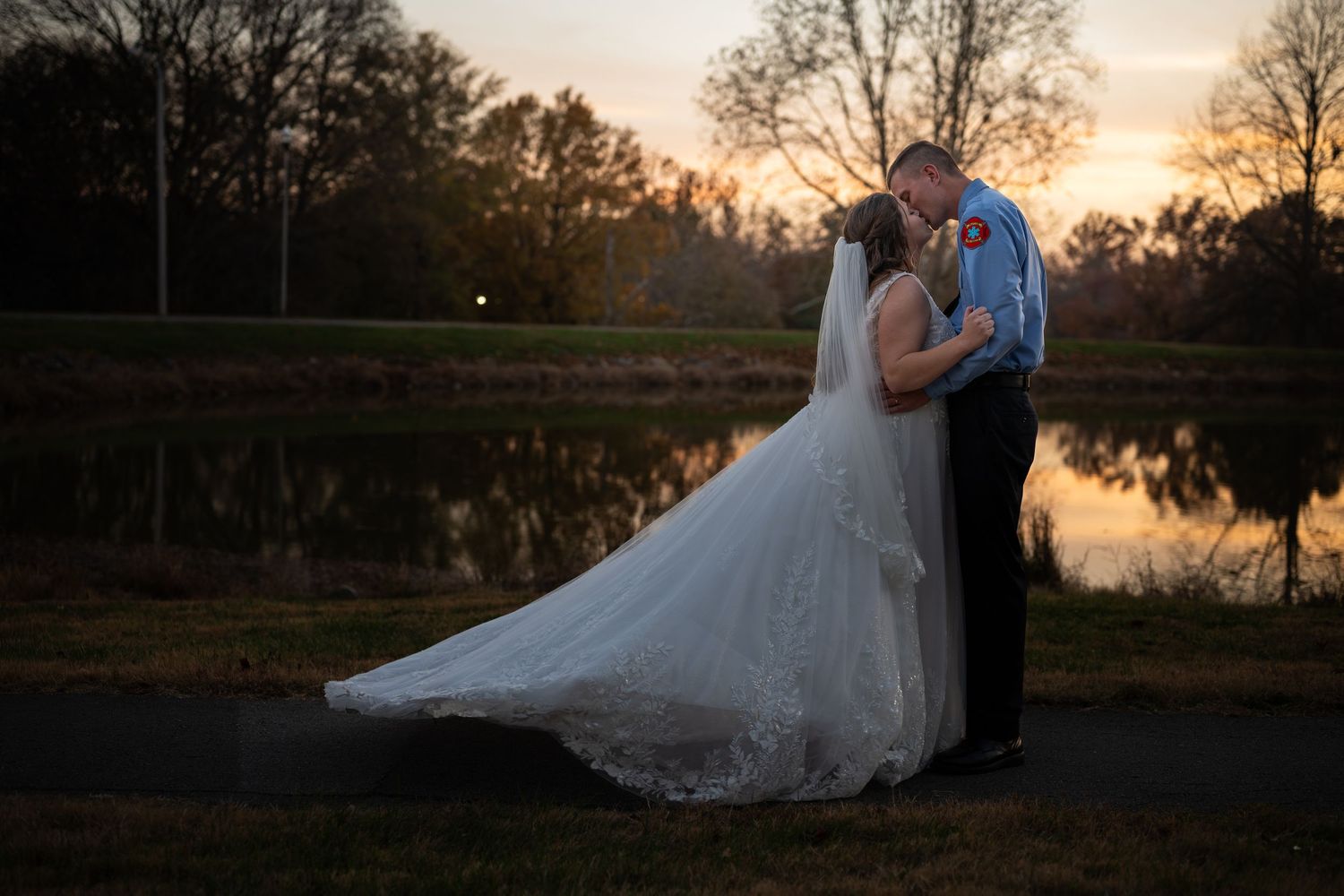 Romantic sunset wedding photos by a lake with silhouettes against orange sky.