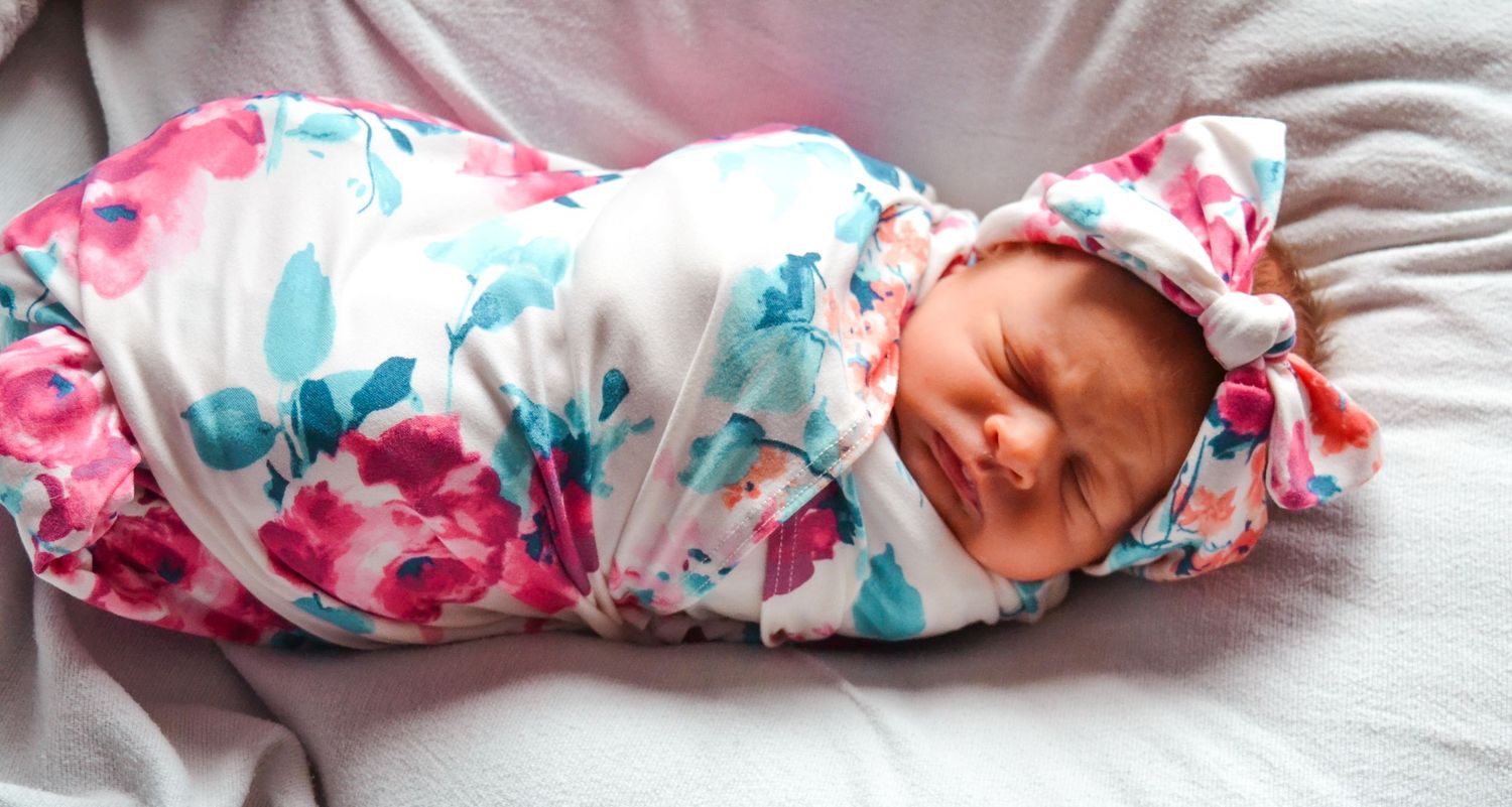 A baby swaddled in floral print blanket lies sleeping in four different positions.