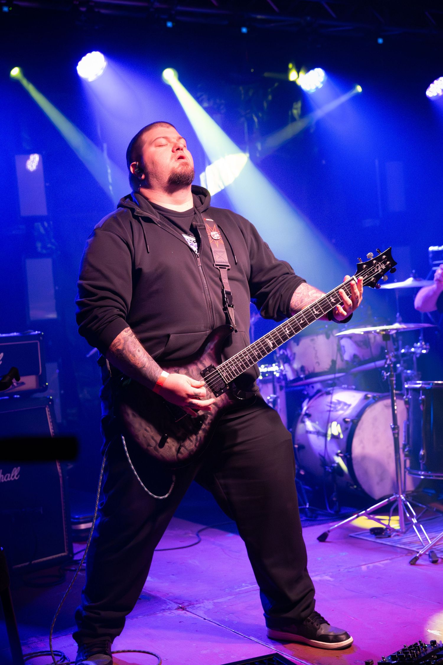 Guitarist performing energetically on stage under bright blue concert lighting.