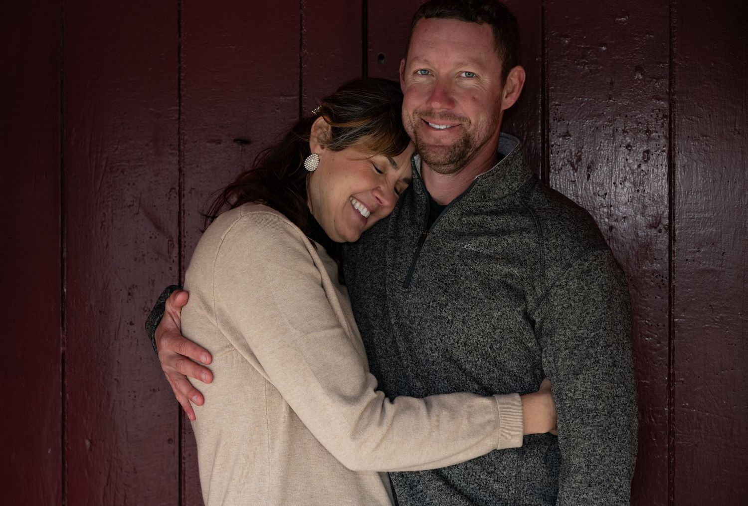 Couple embracing while sitting on wooden bench against dark background.