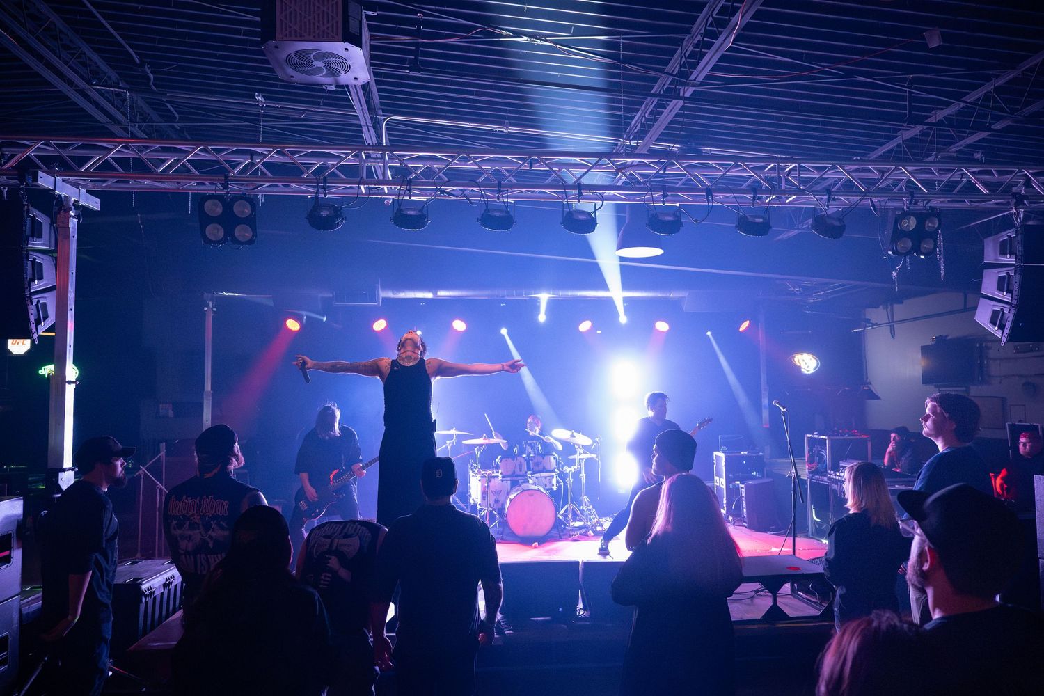 Concert venue illuminated with blue stage lights and fog showing crowd silhouettes in the background.