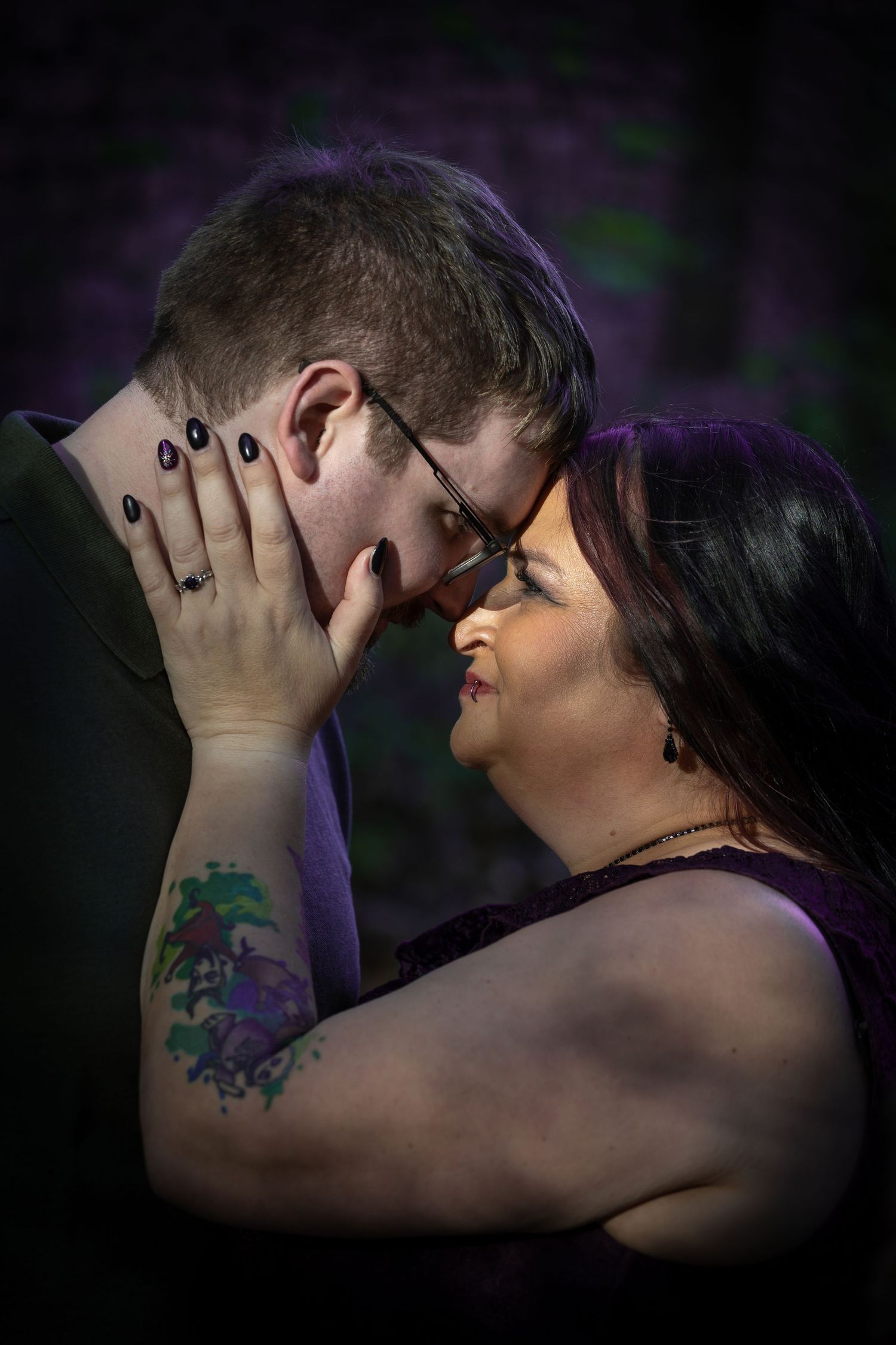 A couple shares an intimate moment in dramatic lighting with dark shadows and purple tones.