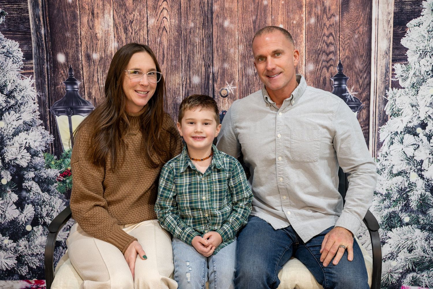 Family poses together on wooden bench surrounded by snowy winter trees and holiday decor in outdoor photo session.