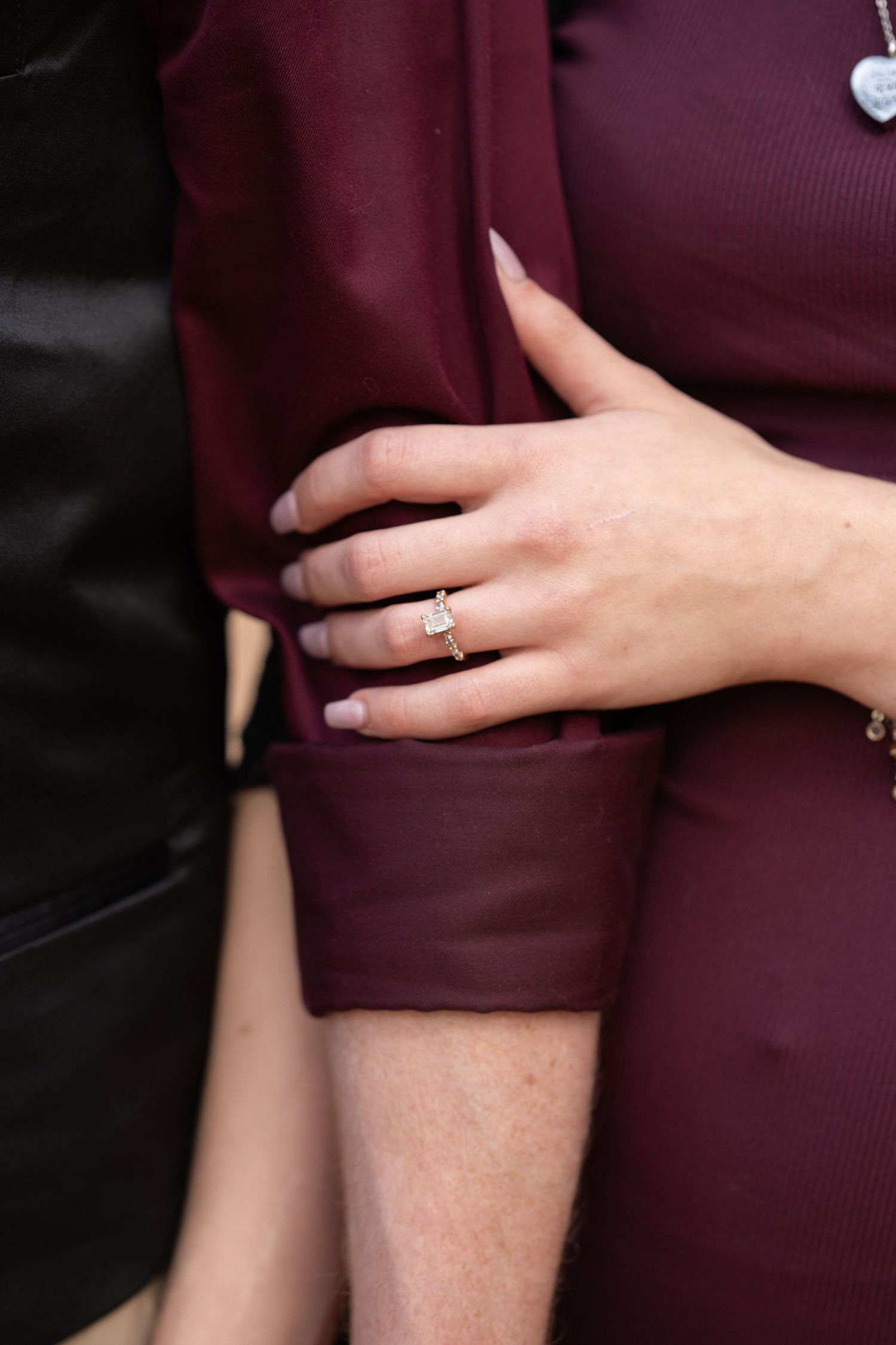 Close-up of a hand wearing an engagement ring with burgundy sleeve detail.
