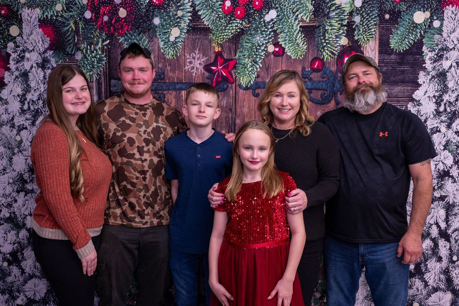 Family portrait with festive floral backdrop featuring red flowers and holiday decorations.
