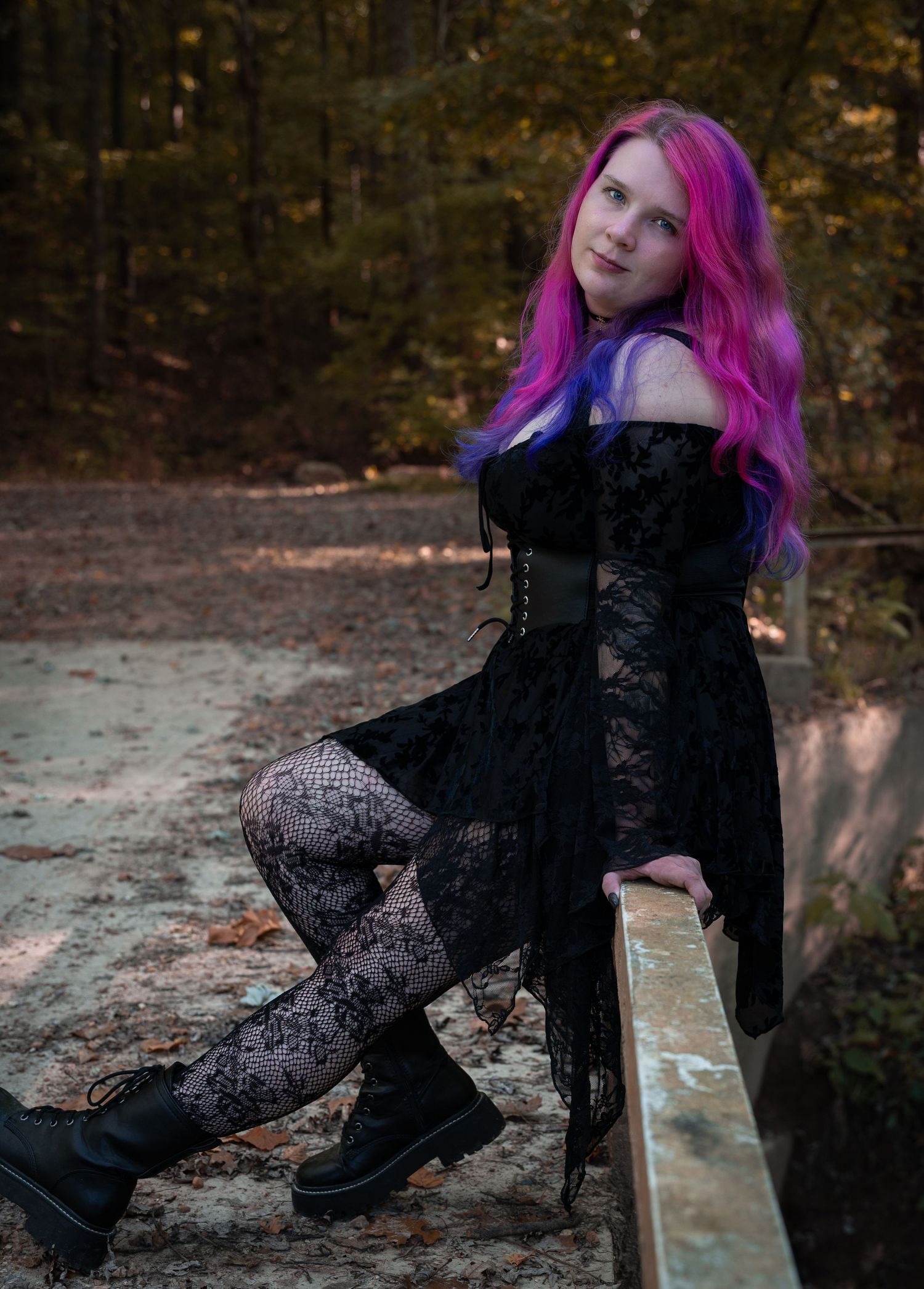 Gothic style outfit with black lace dress, patterned tights and boots against autumn forest backdrop.