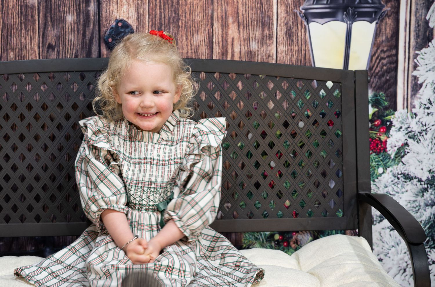 Rustic holiday photo setup with lanterns and lattice bench against wooden wall.