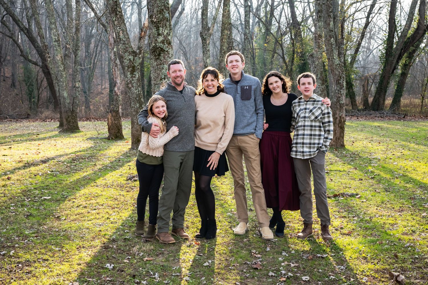 Family group poses outdoors among bare trees and fallen yellow leaves.
