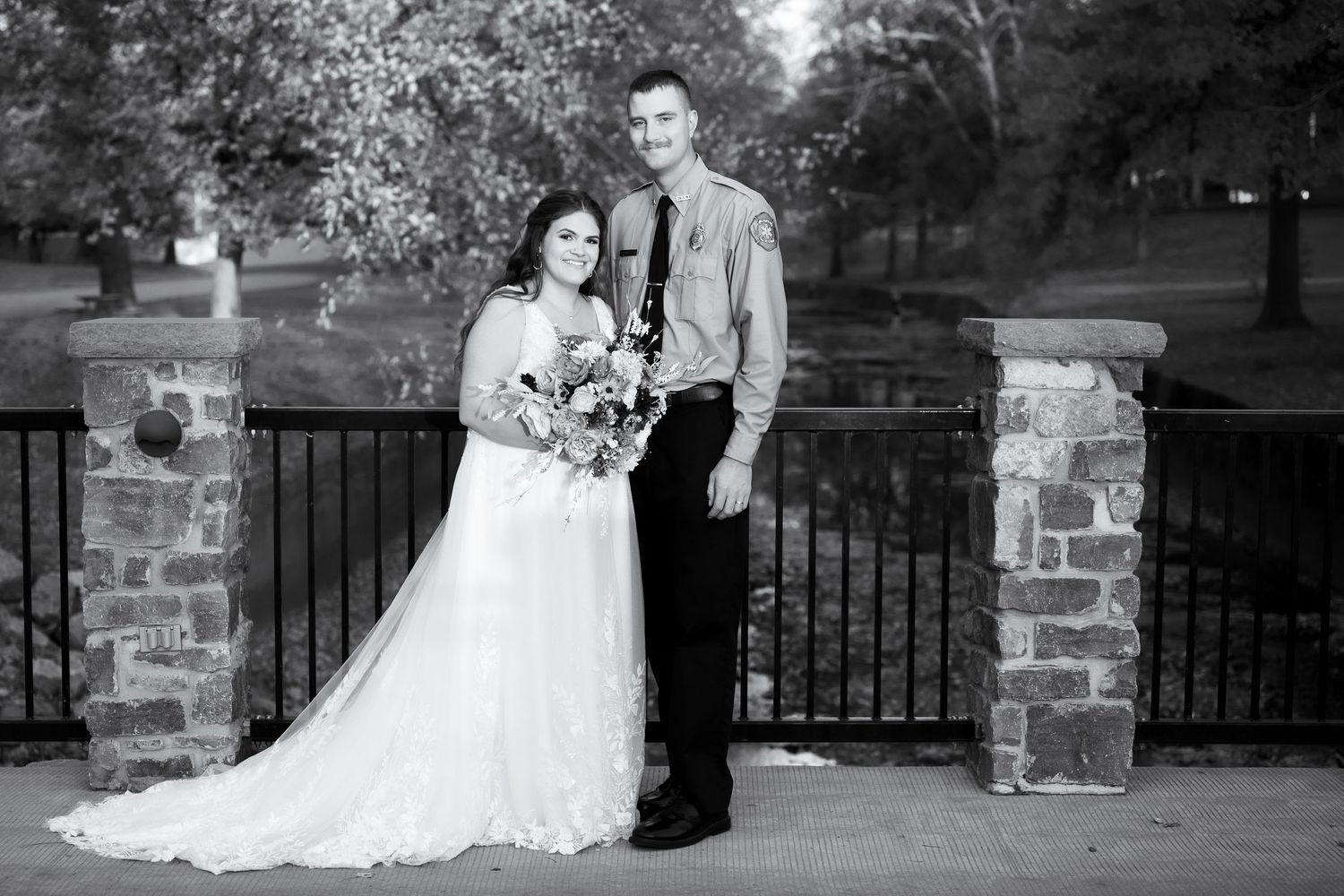 Elegant wedding portraits taken against rustic stone wall and iron fence backdrop.