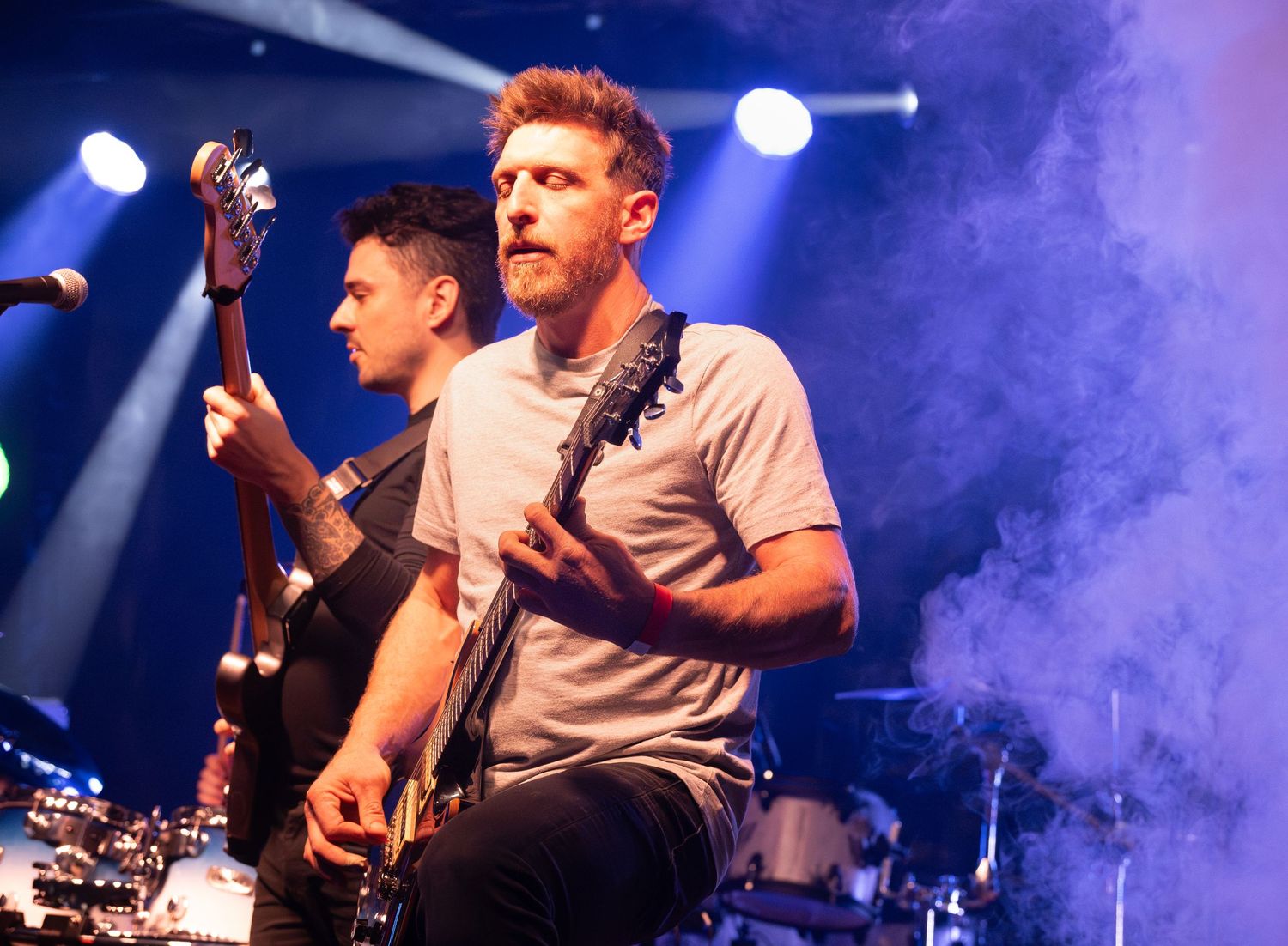 Musicians performing on stage with dramatic concert lighting and smoke effects.