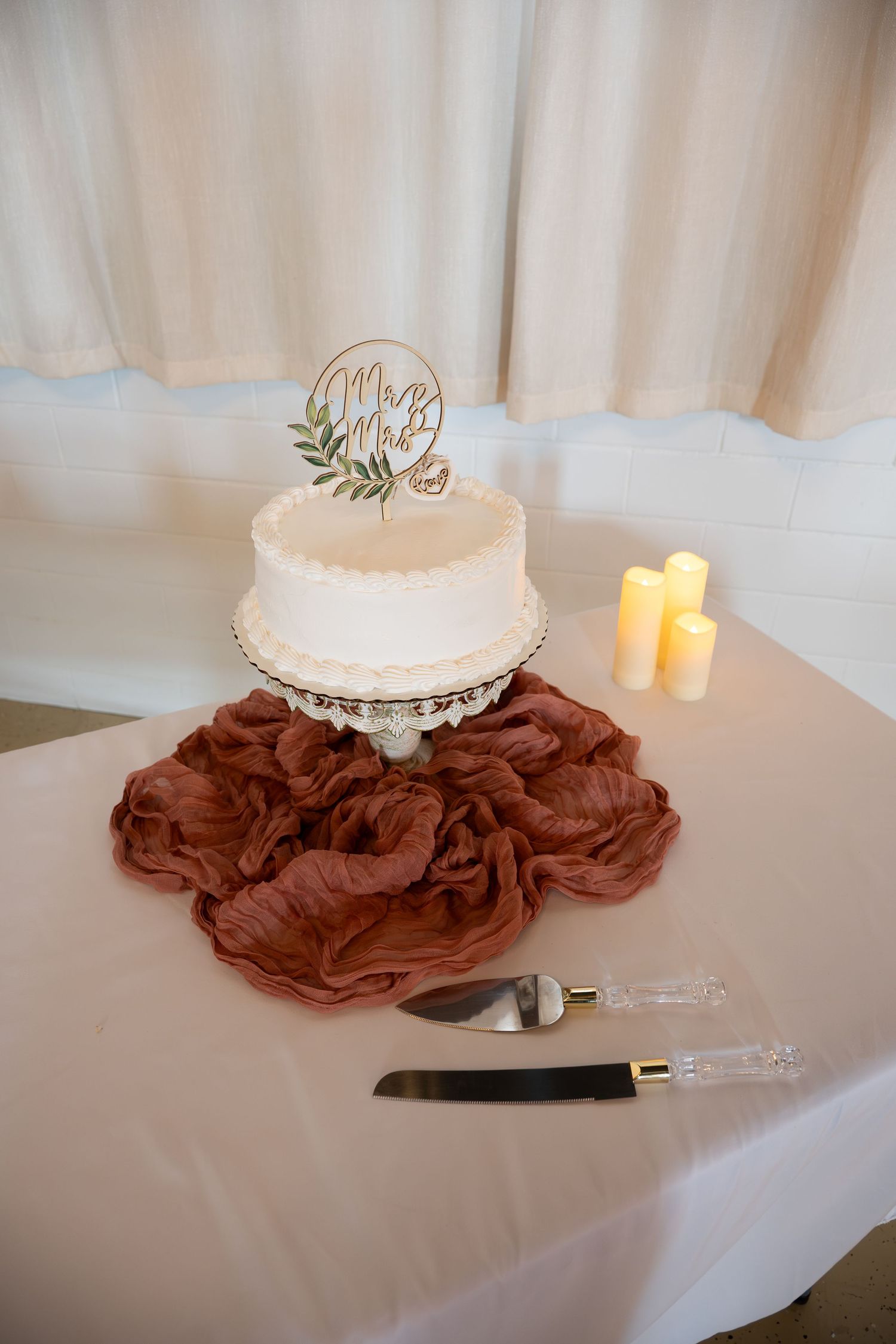 White wedding cake displayed on a table with burgundy fabric accents and candles.
