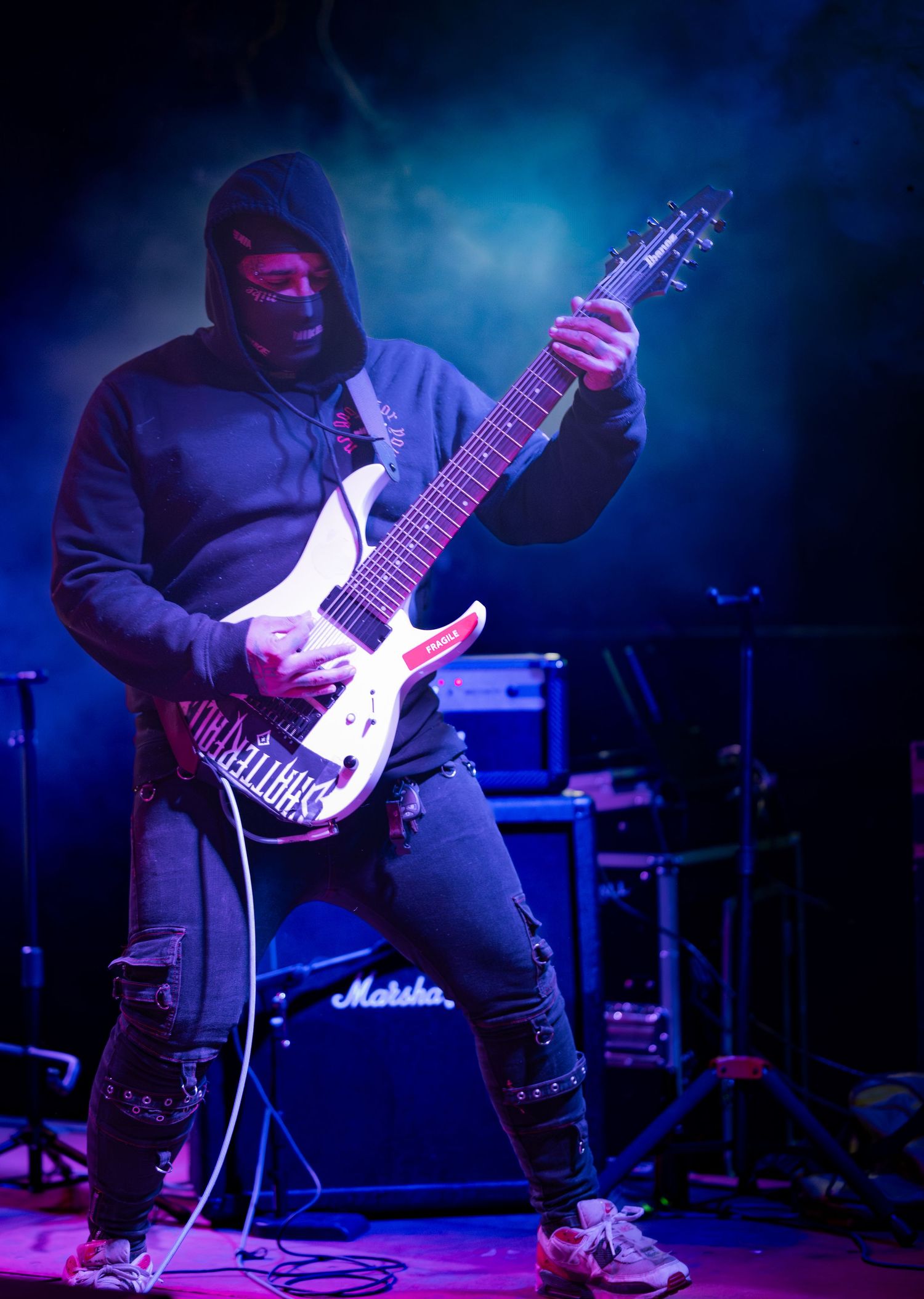 Guitarist performs on stage with electric guitar under dramatic blue and purple lighting during live concert performance.