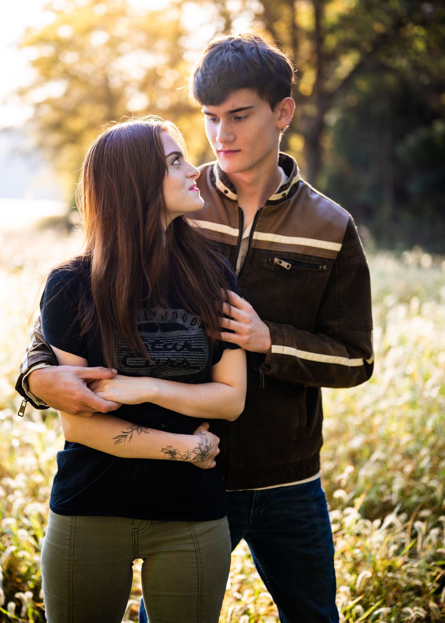 A couple embraces tenderly in a sunlit meadow during golden hour, creating a romantic silhouette against nature.