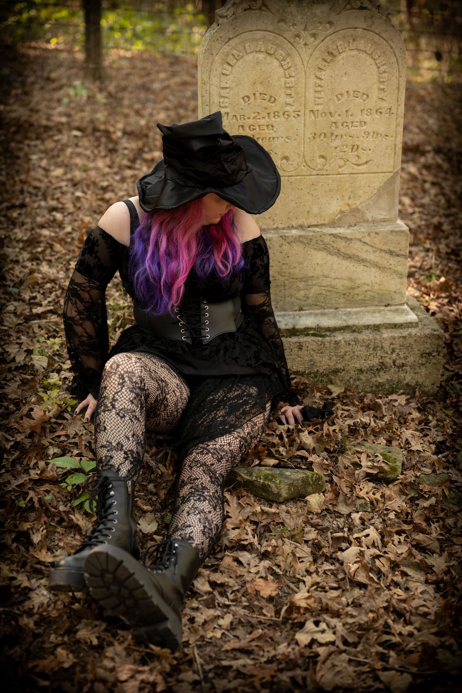 Gothic boots and lace stockings against fallen autumn leaves with an old cemetery headstone in the background.