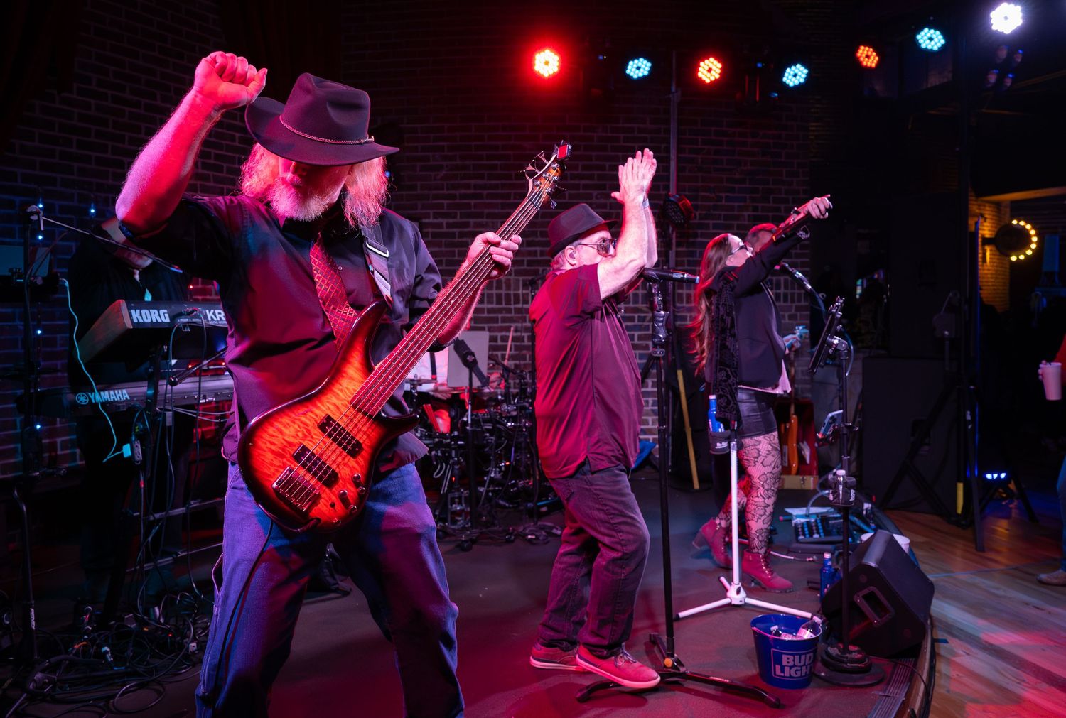 Musicians perform on stage with colorful stage lighting and instruments during a live concert performance.