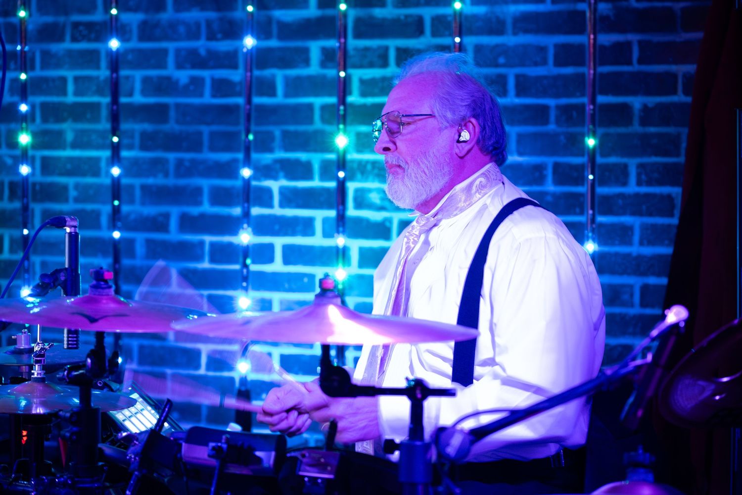 A musician performs on stage under blue and purple lighting while playing a keyboard instrument.