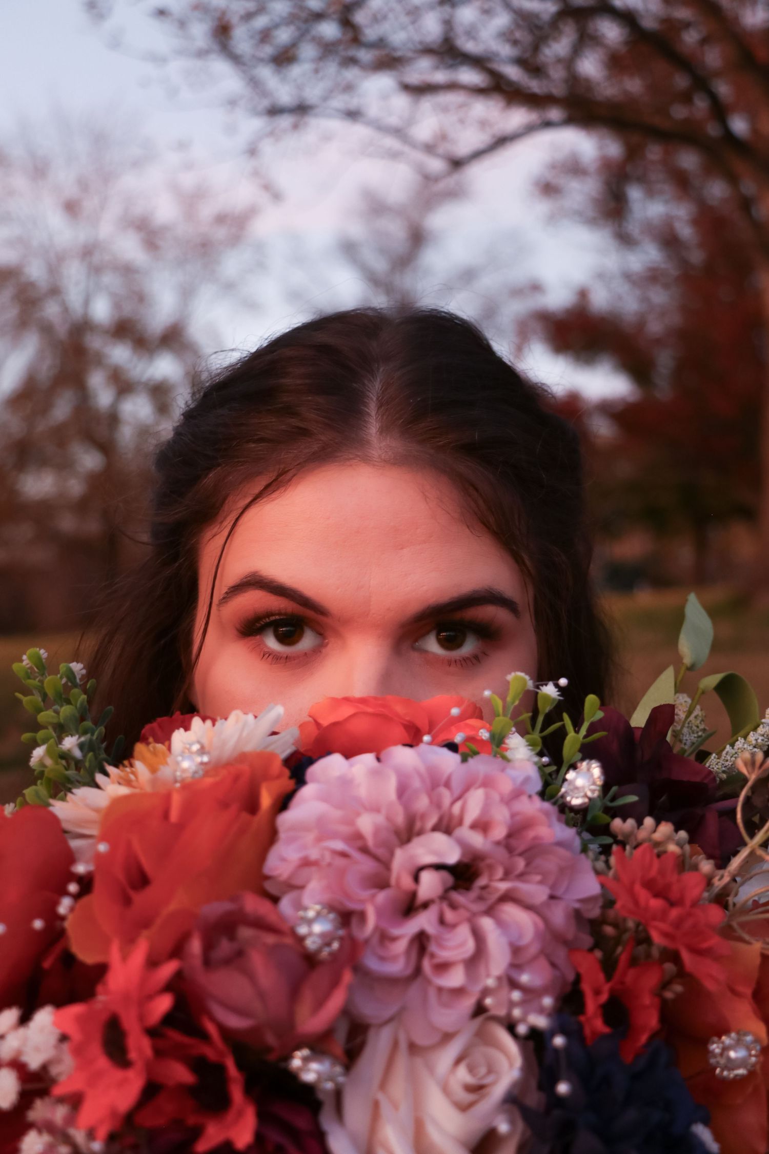 Playful bridal portrait peeking over colorful autumn flower bouquet.