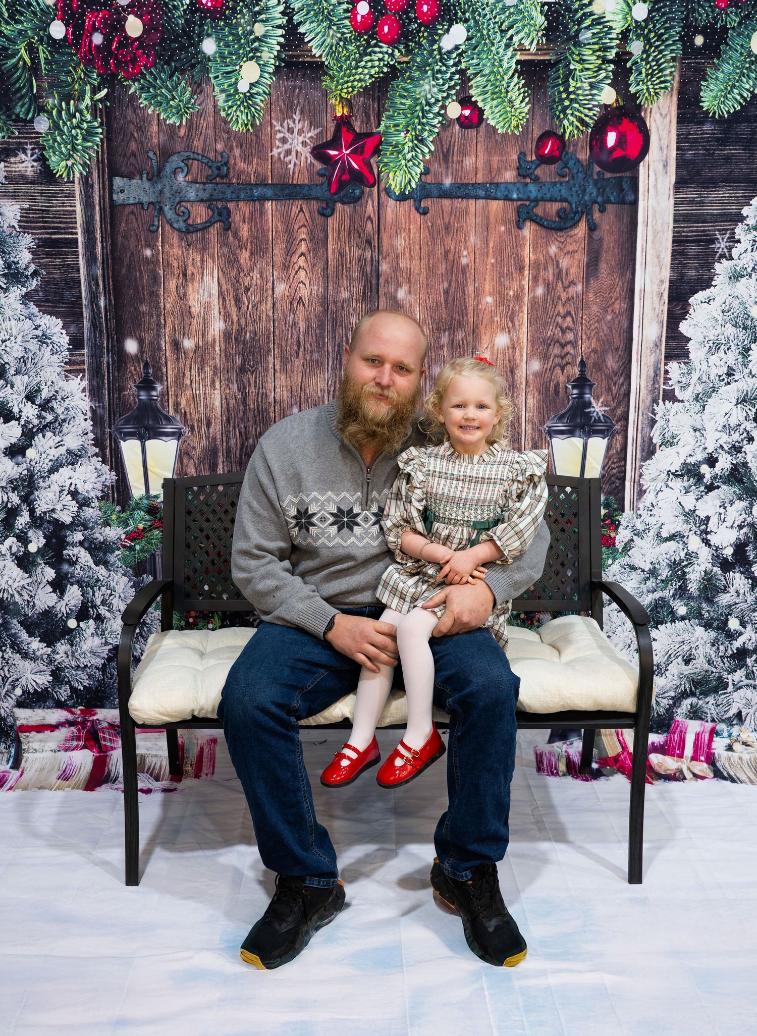 Cozy Christmas photo setup with decorated evergreens, wooden wall and festive ornaments.