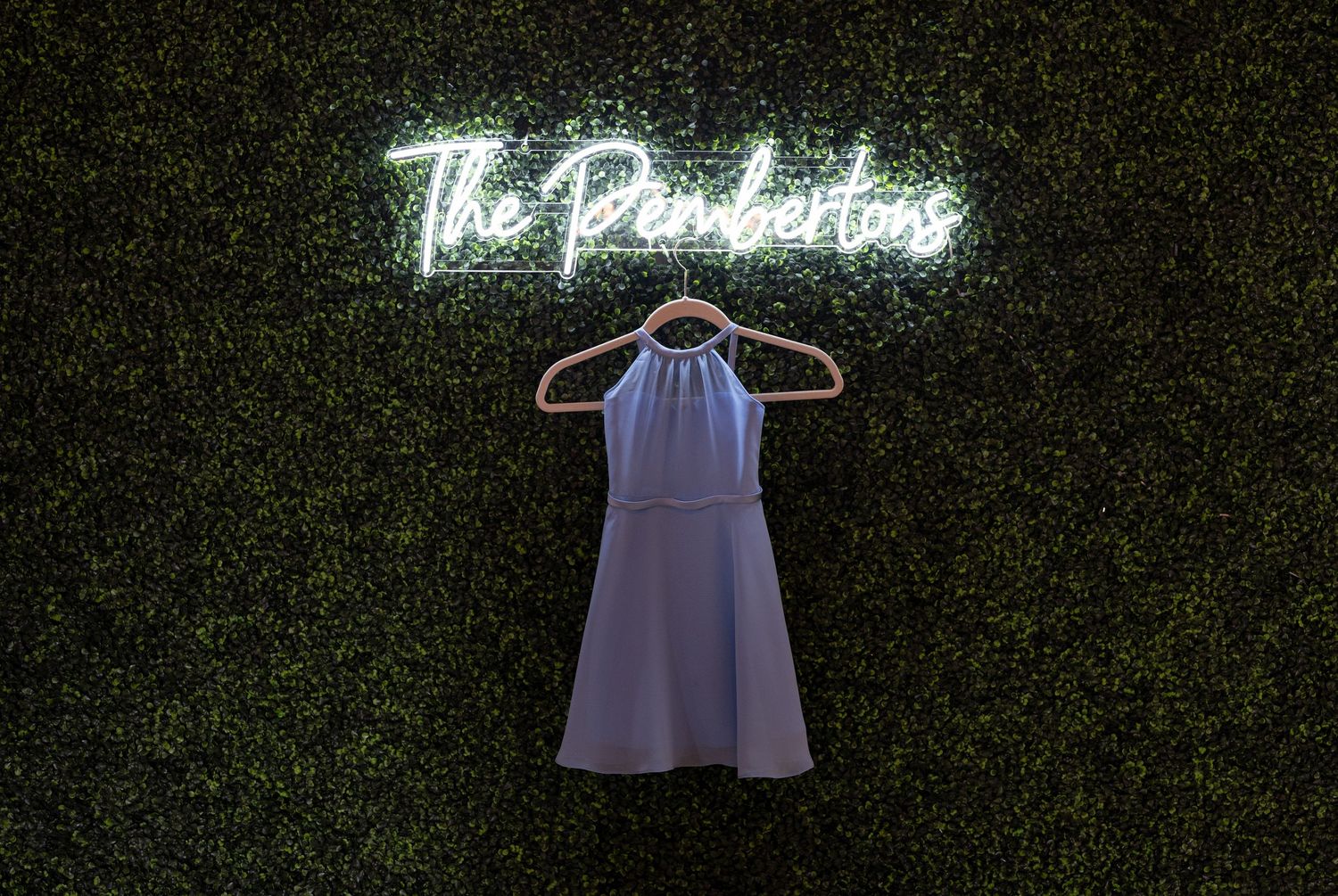 White wedding dress displayed against a dark green hedge wall with neon signage.