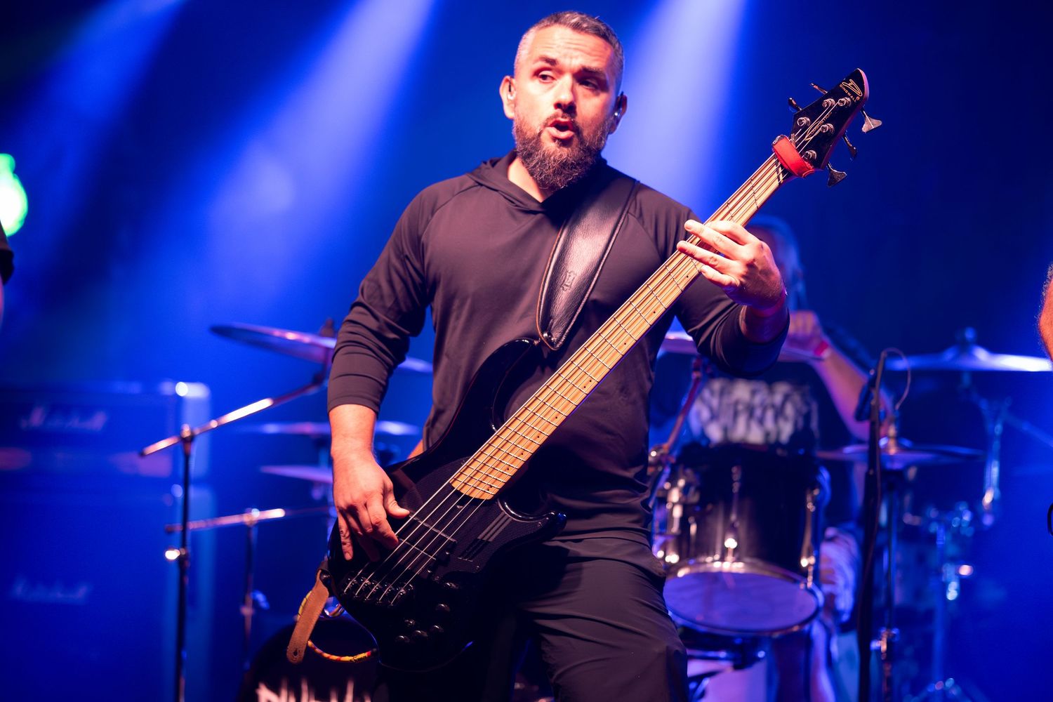 Musicians playing bass guitars perform under dramatic blue stage lighting at a rock concert.