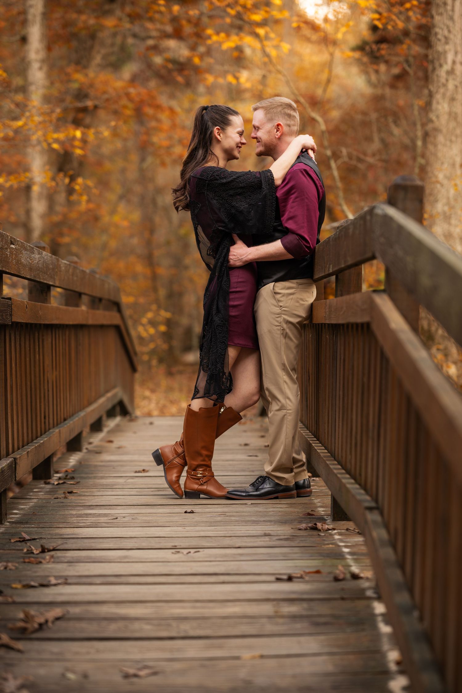 Romantic couple embraces on wooden bridge surrounded by autumn foliage in golden afternoon light.