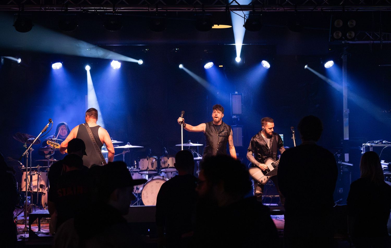 Musicians perform on a dark stage with dramatic blue lighting and spotlights during a live concert performance.