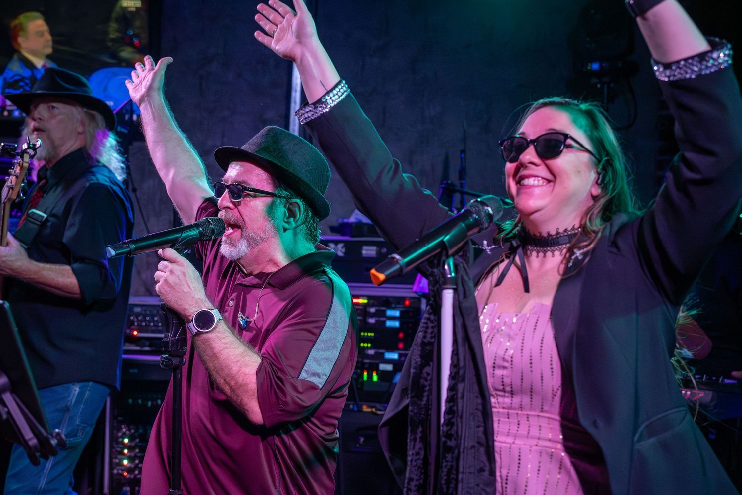 Musicians perform together on stage under colorful lighting at a live concert venue.