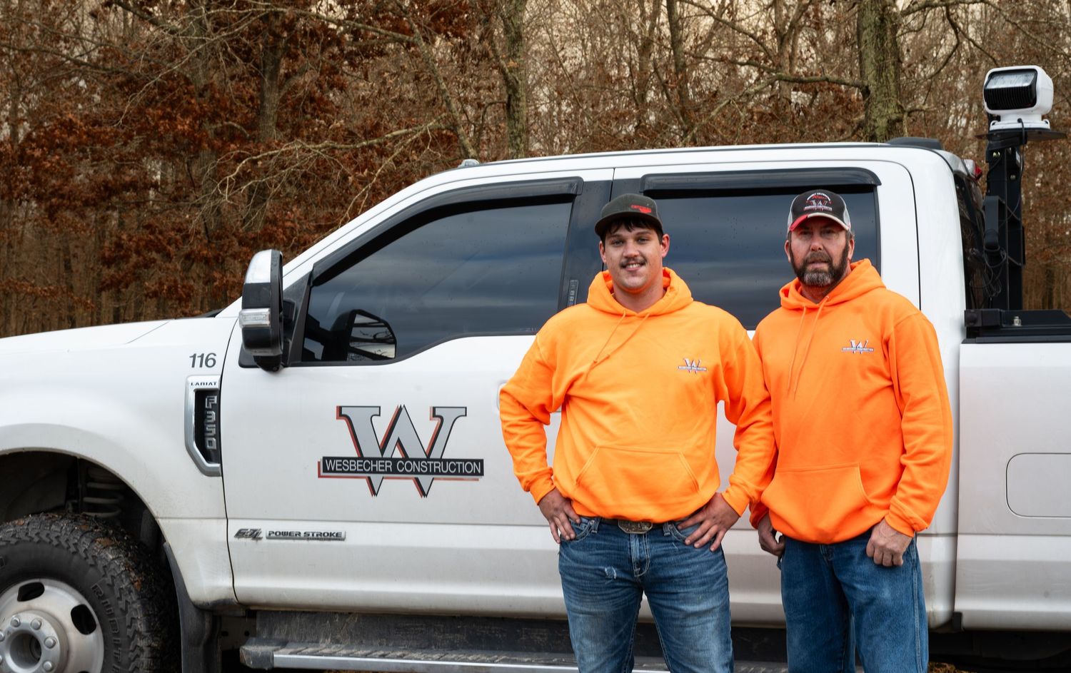 Workers in orange safety vests and casual wear gathered by company vehicles.