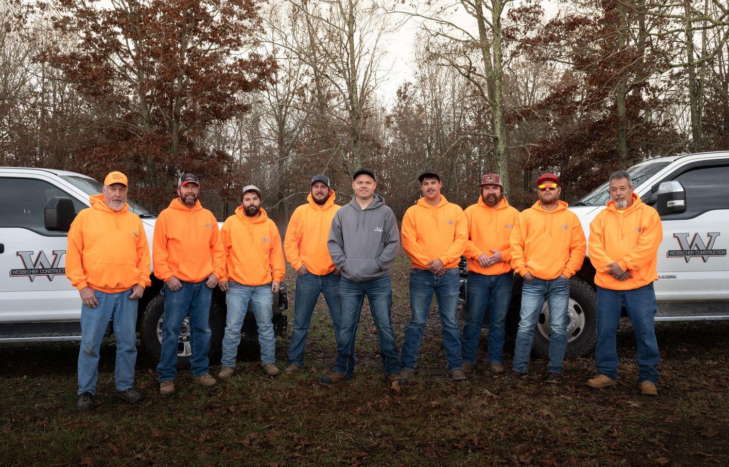 Group of workers in high-visibility orange jackets lined up outdoors in autumn setting.
