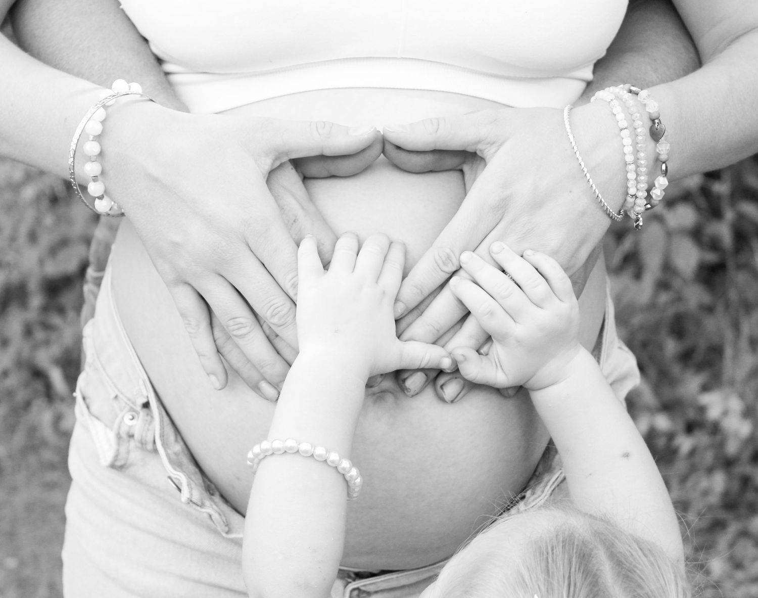 A series of black and white maternity photos showing close-up details of pregnant bellies and hands in tender poses.
