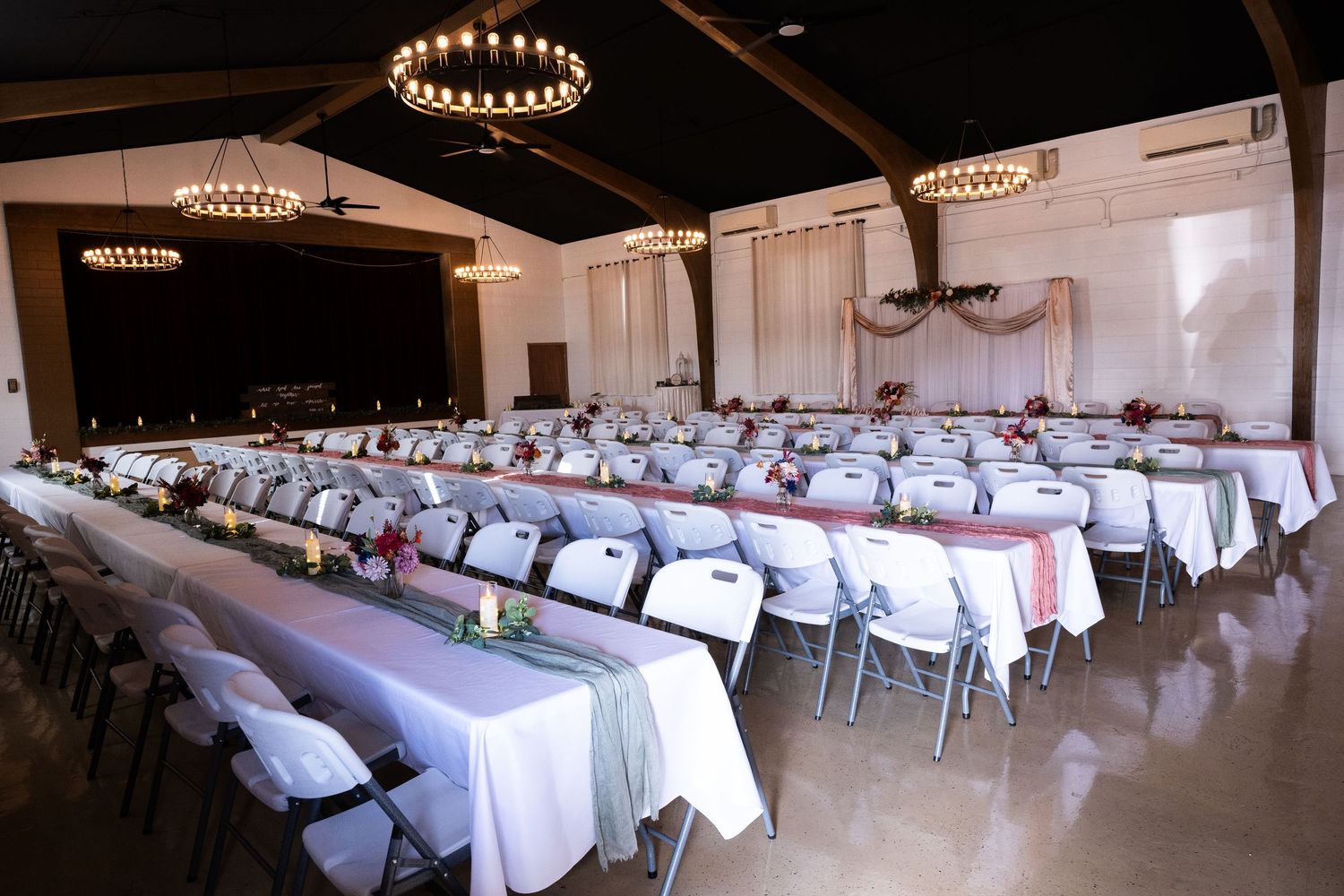 Large banquet hall set up with round tables and white linens under elegant chandeliers.