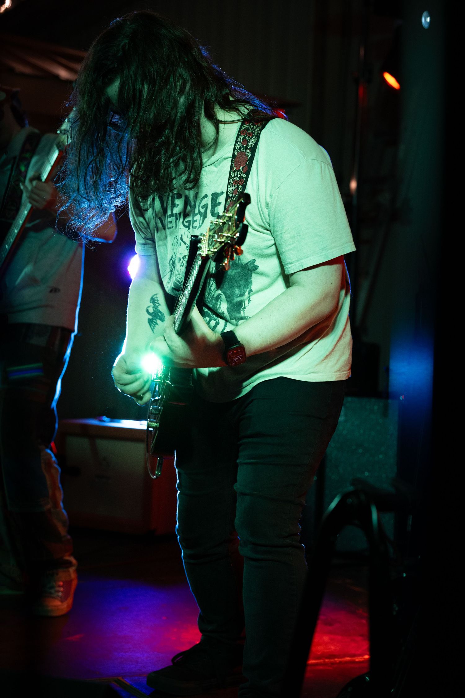 Musician performing on stage in dark lighting with dramatic blue and green spotlights creating moody atmosphere.